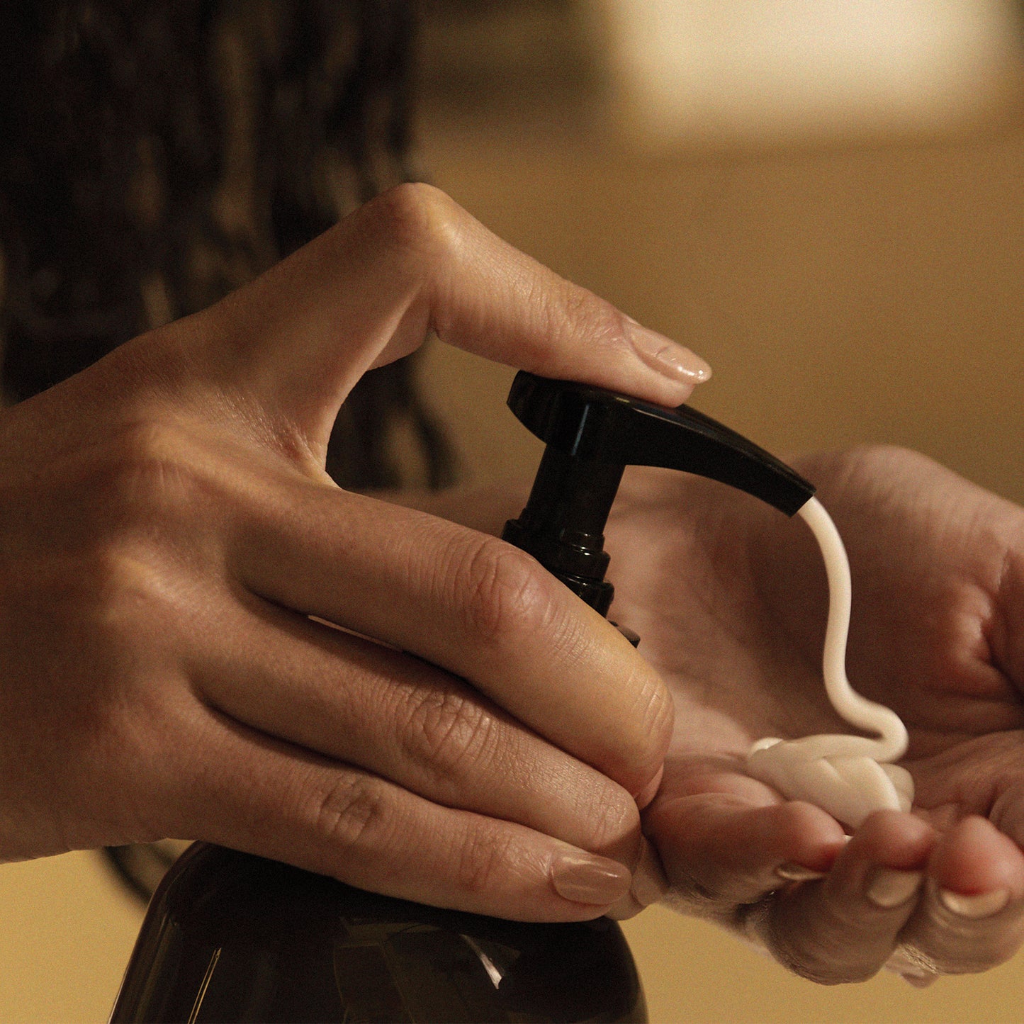 A person moisturising their hands using Ashley and Co 'Sootherup' hand and body lotion in blossom and gilt fragrance.
