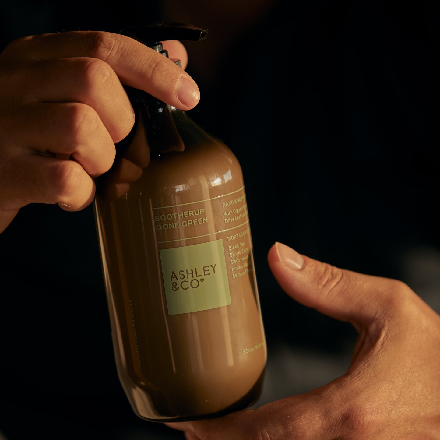 A man holding a bottle of Ashley and Co 'Sootherup Gone Green' hand and body lotion in mortar and pestle fragrance.
