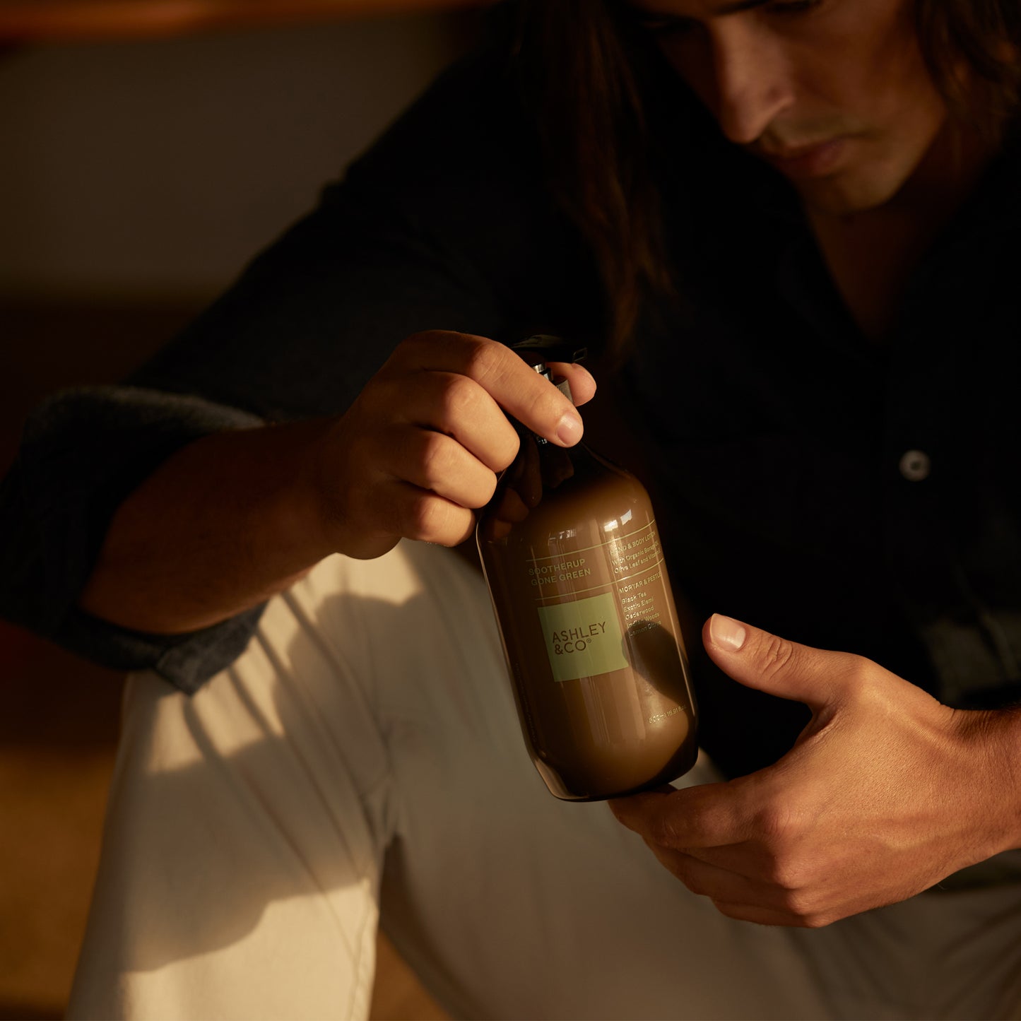 A man holding a bottle of Ashley and Co 'Sootherup Gone Green' hand and body lotion in mortar and pestle fragrance.