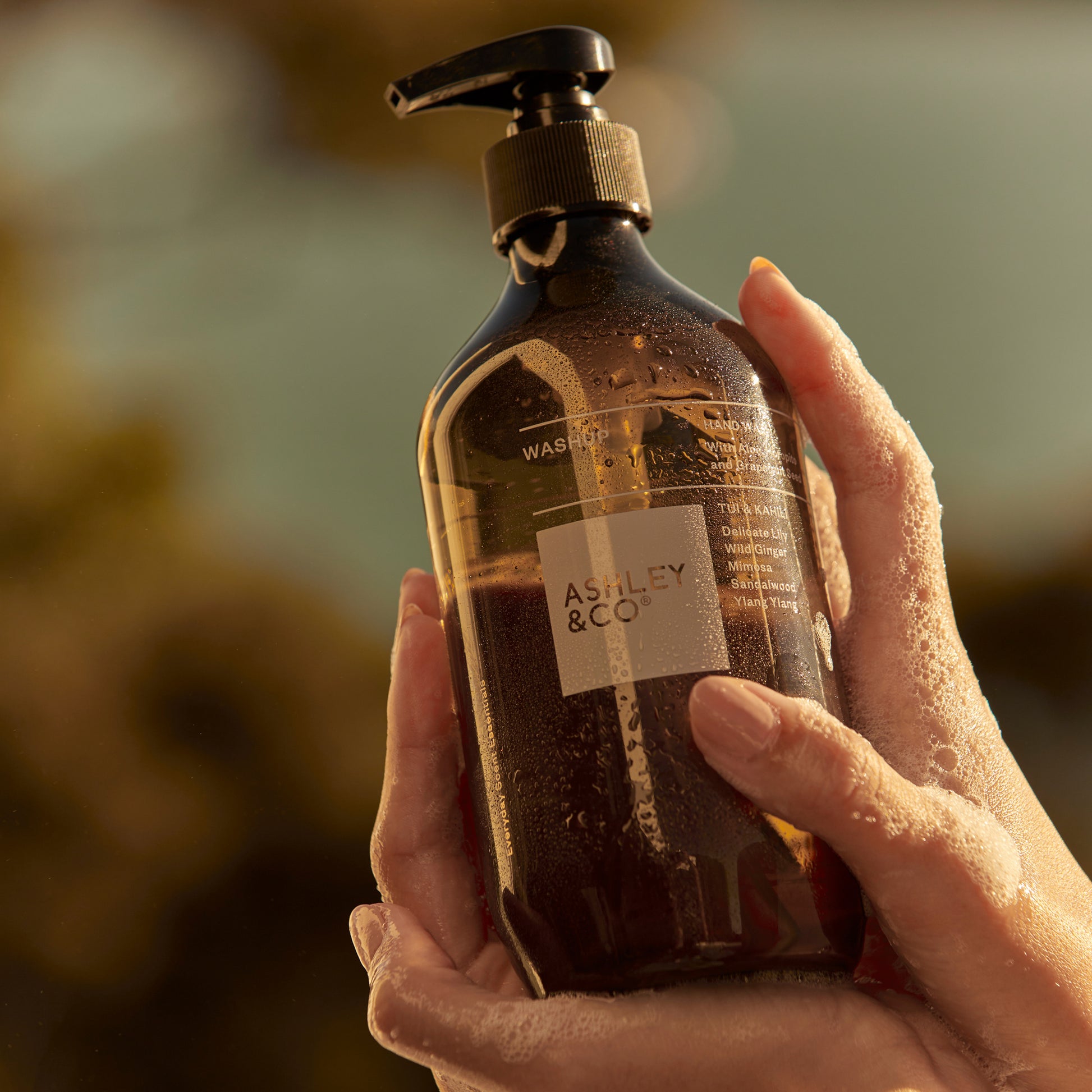 Ashley and Co 'Washup' handwash in Tui and kahili fragrance held by hands covered in soap suds.