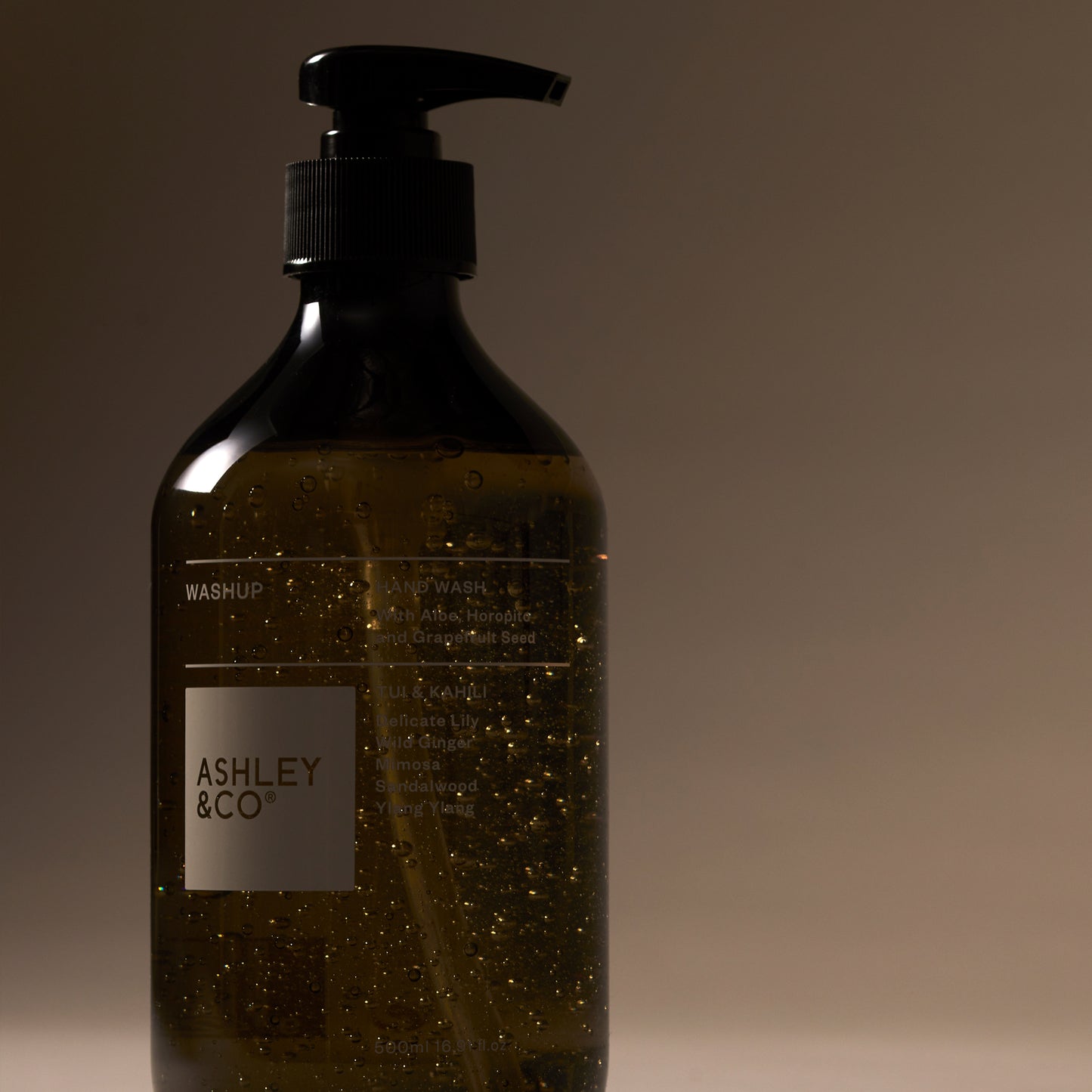 Close up of front Ashley and Co 'Washup' handwash in Tui and kahili fragrance on grey background.