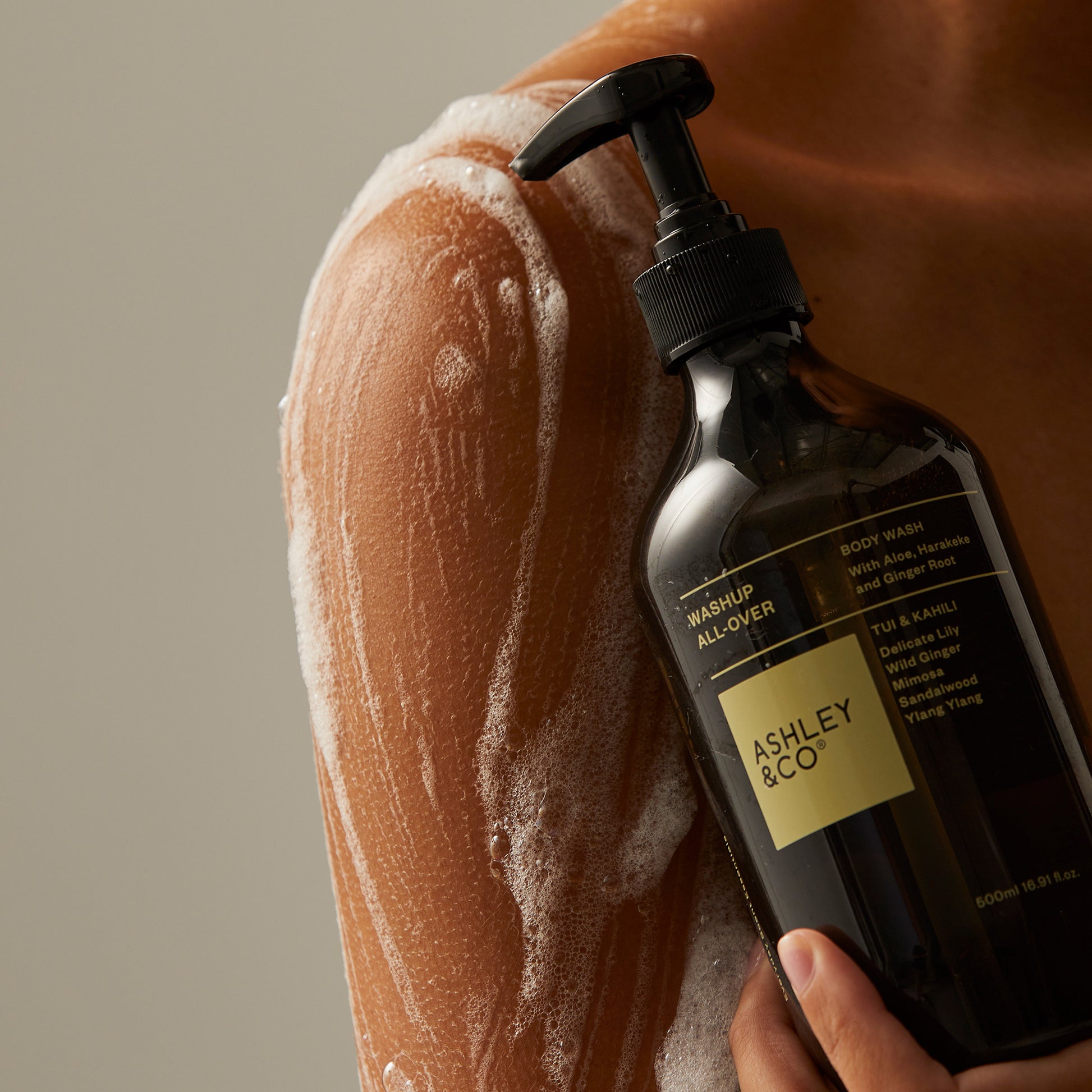 Close up of Ashley and Co 'Washup All Over' body wash in tui and kahili fragrance in the shower with soap suds and a woman's body.