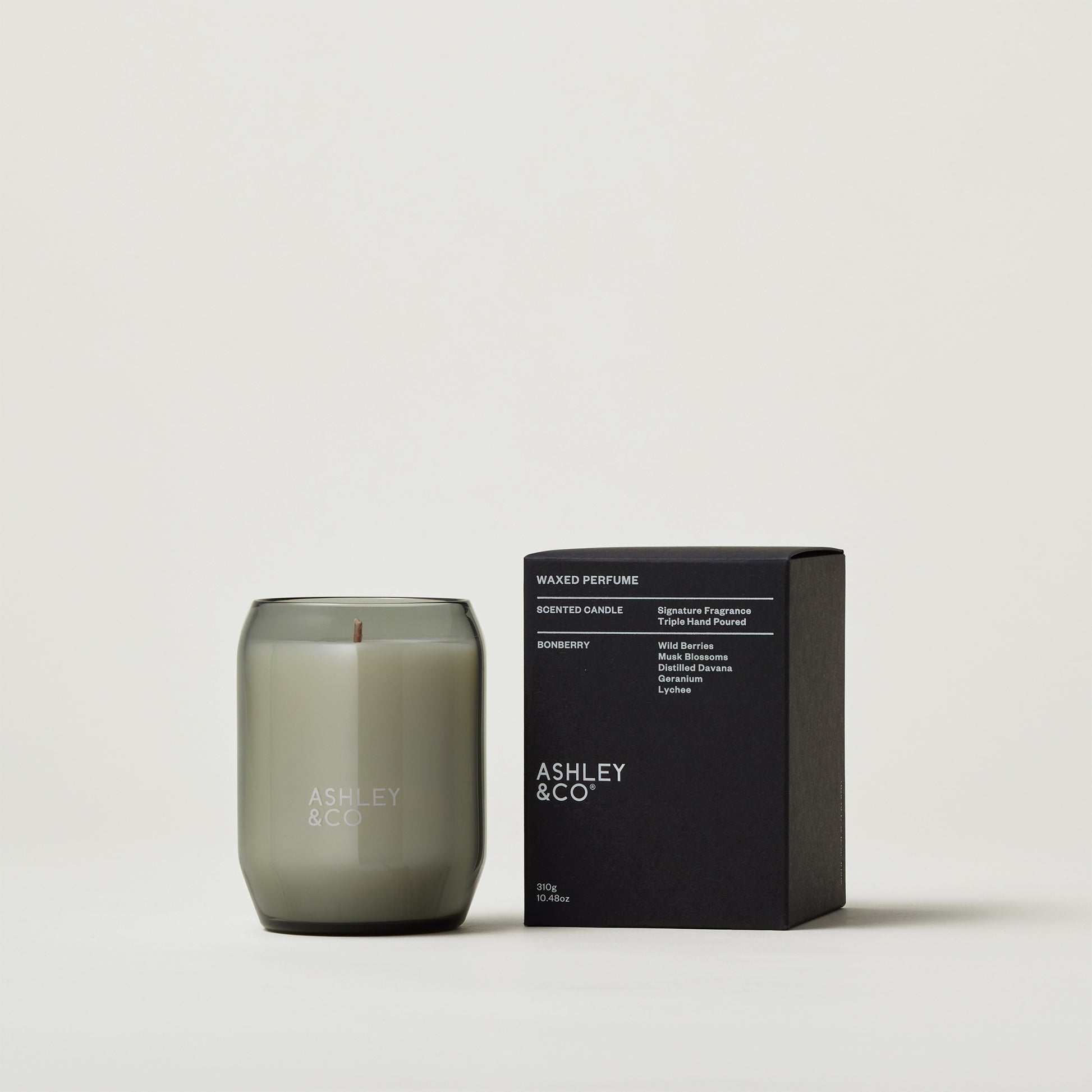 Close up of a woman sitting next to an Woman sitting next to Ashley and Co 'Waxed Perfume' scented candle in bonberry fragrance.