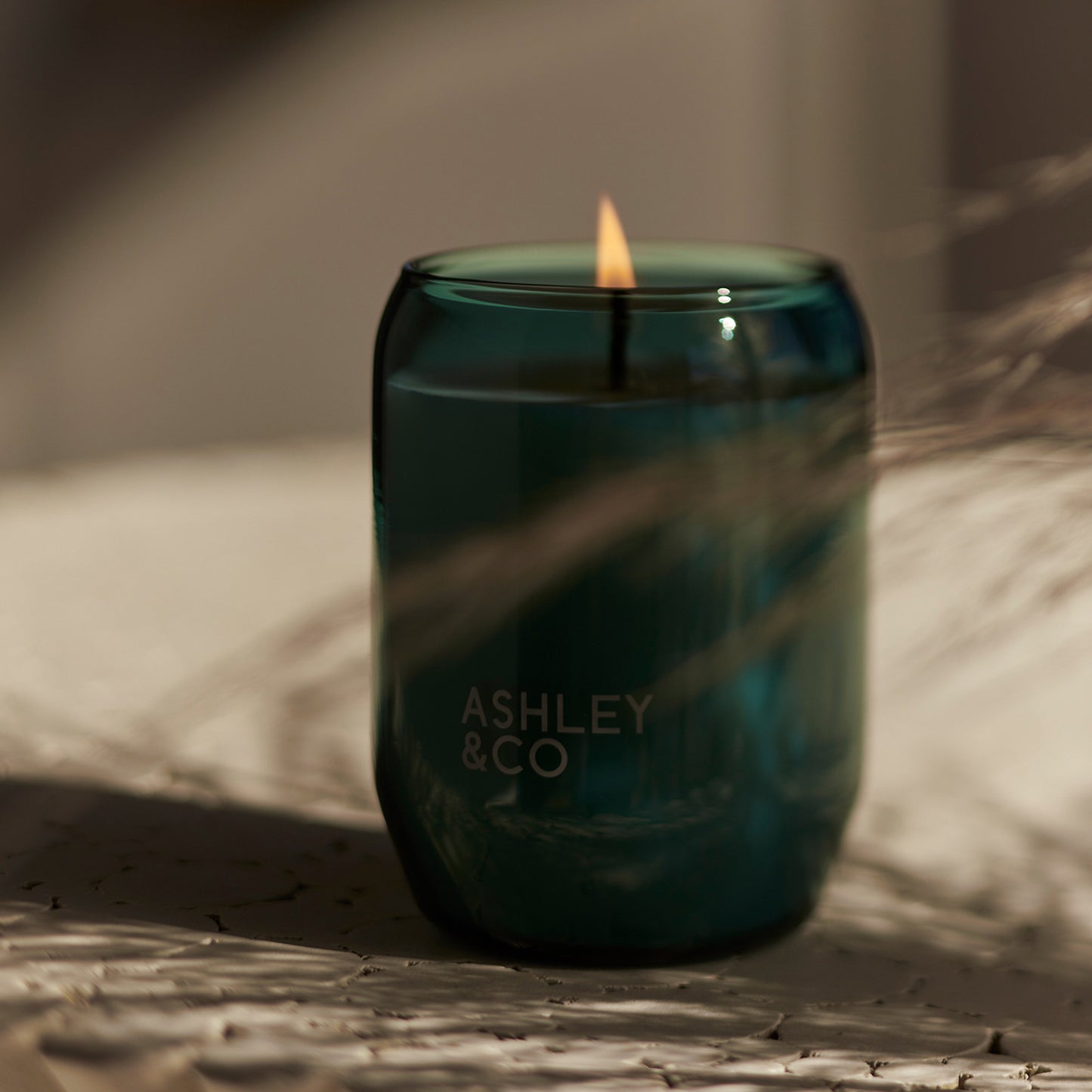 Close up of green glass Ashley and Co 'Waxed Perfume - Outdoor Edition' scented candle in tui and kahili fragrance.