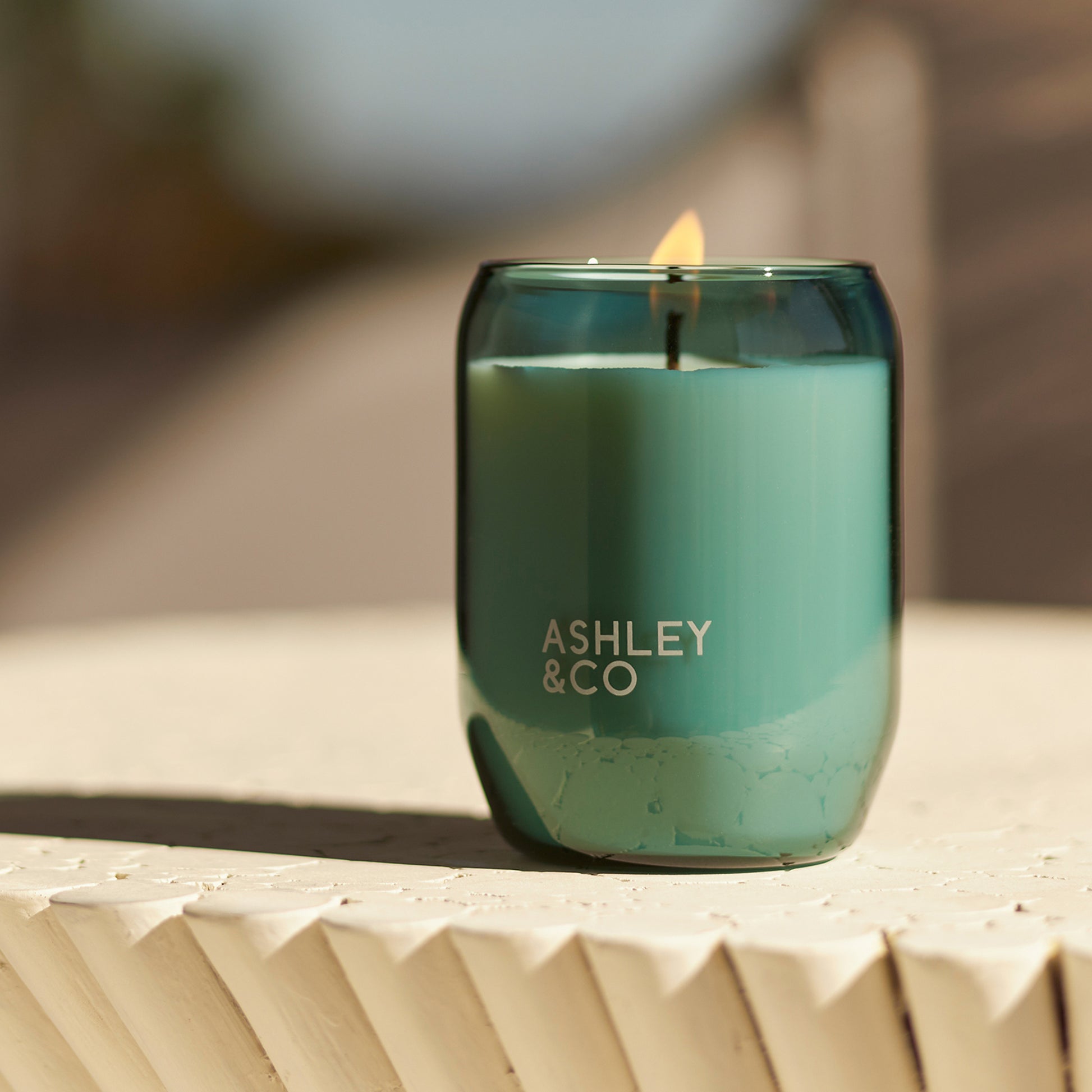 Close up of green glass Ashley and Co 'Waxed Perfume - Outdoor Edition' scented candle in tui and kahili fragrance.