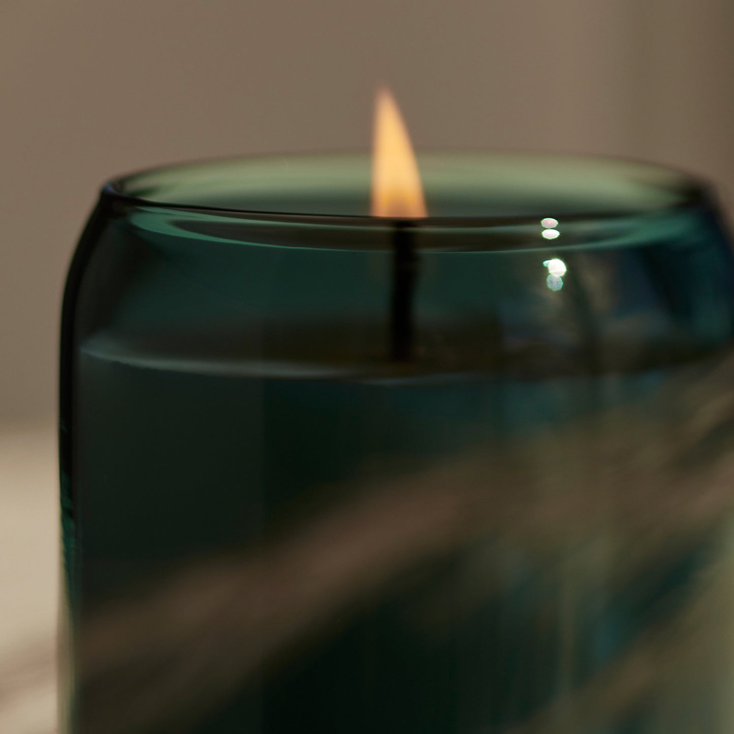 Detailed flame burning image green glass Ashley and Co 'Waxed Perfume - Outdoor Edition' scented candle in tui and kahili fragrance.