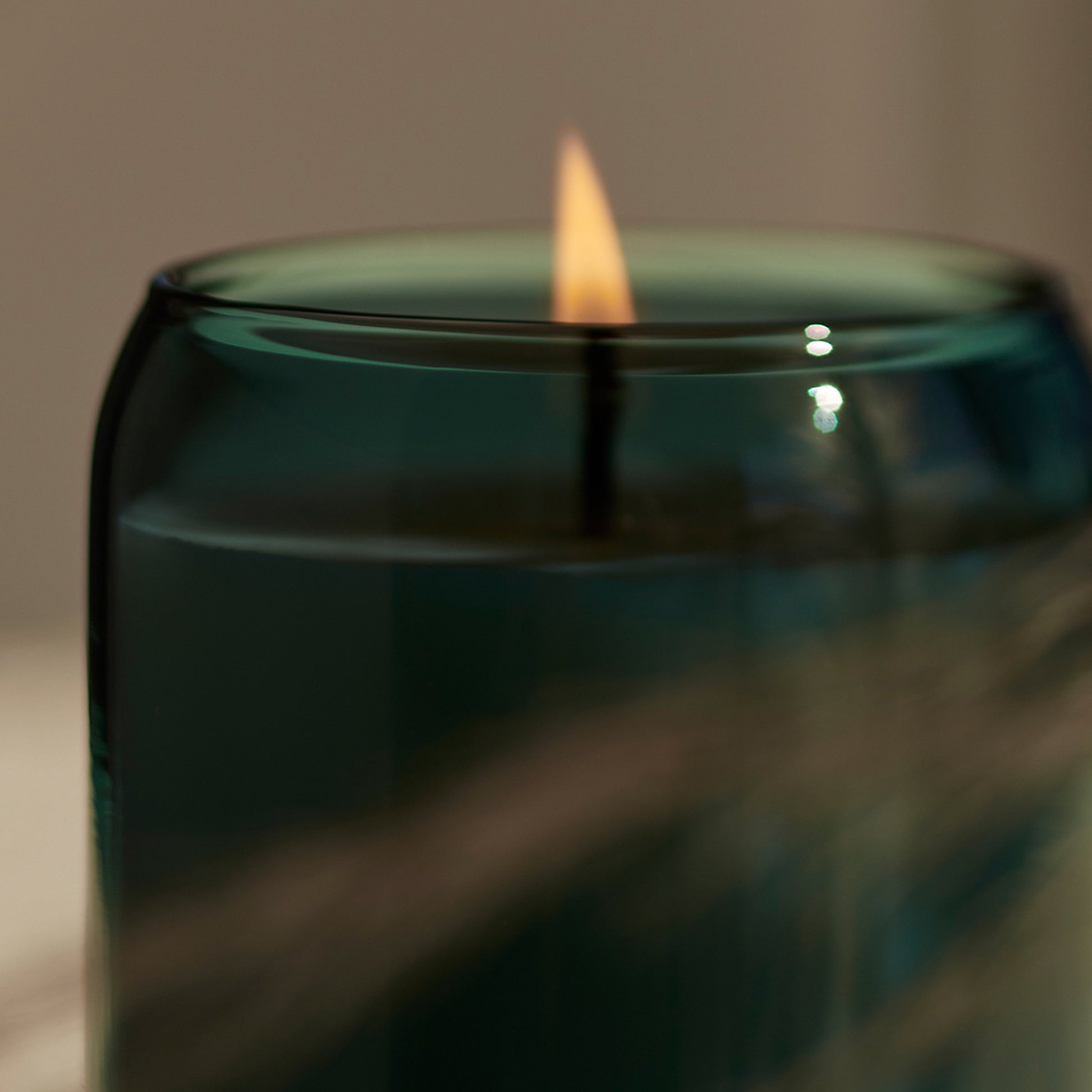 Detailed flame burning image green glass Ashley and Co 'Waxed Perfume - Outdoor Edition' scented candle in tui and kahili fragrance.