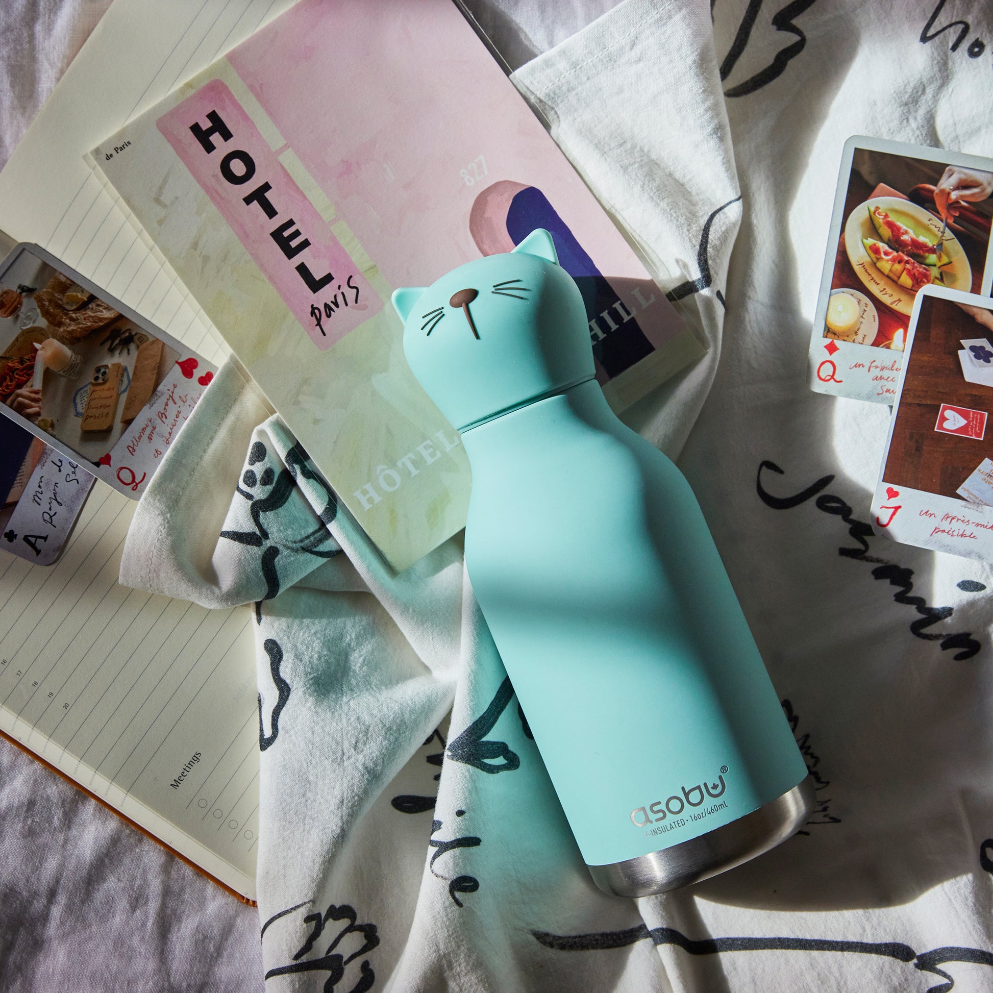 Image of Cat Bestie Bottle by Asobu, shown lying on note books,