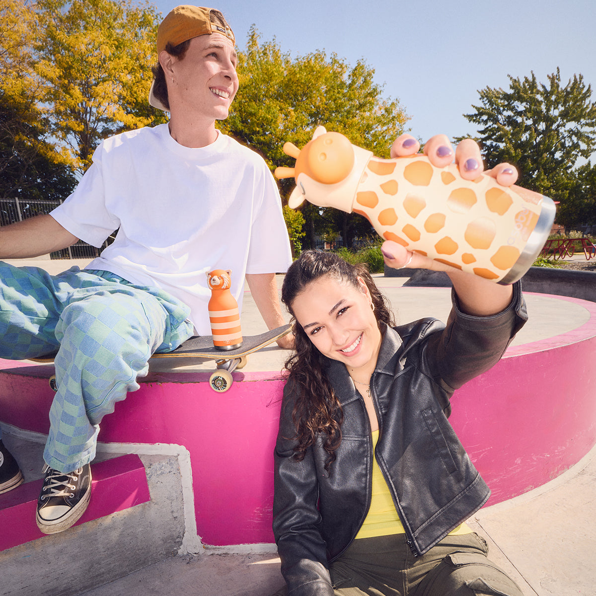 A Giraffe Bestie Bottle by Asobu being held above a girl's head in a skate park.