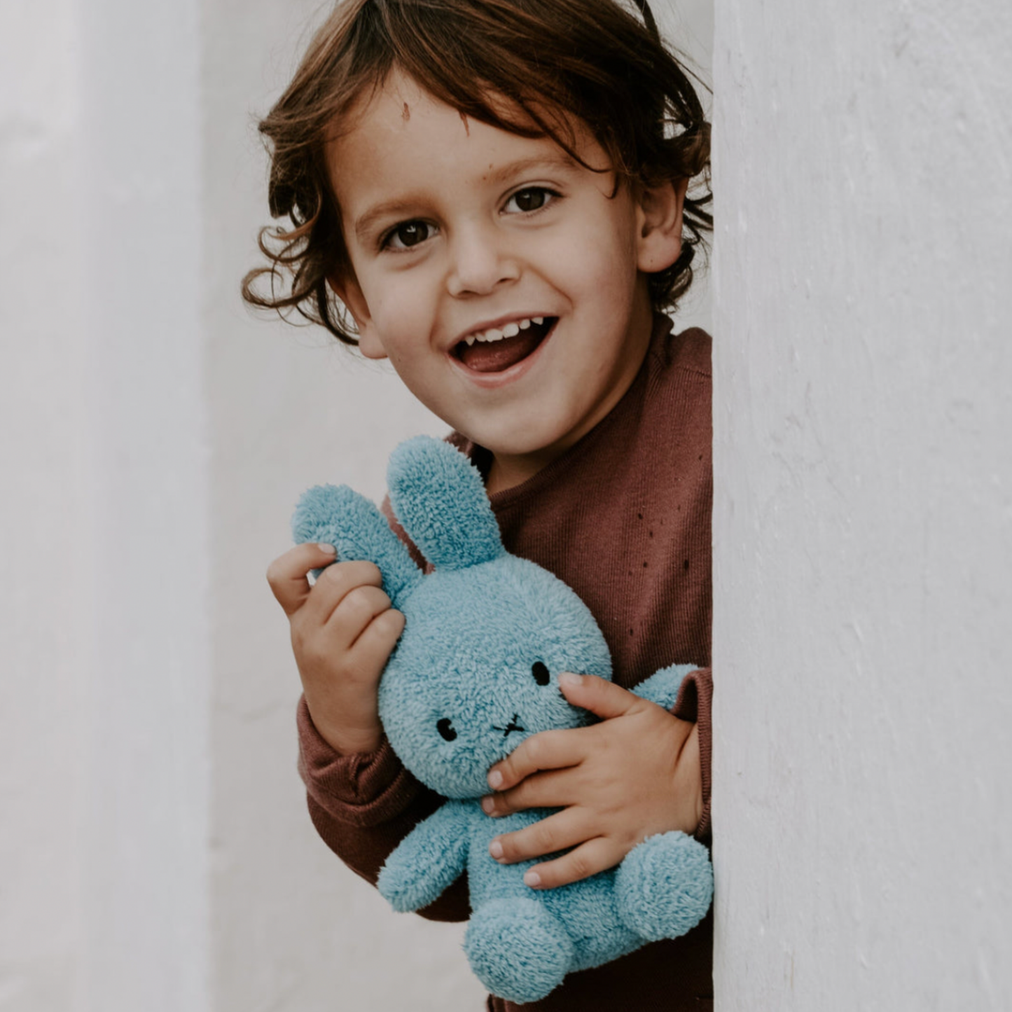 Child with light blue terry Sitting Miffy 23cm peering around coner with BonTon Toys Miffy in hand lifestyle shot