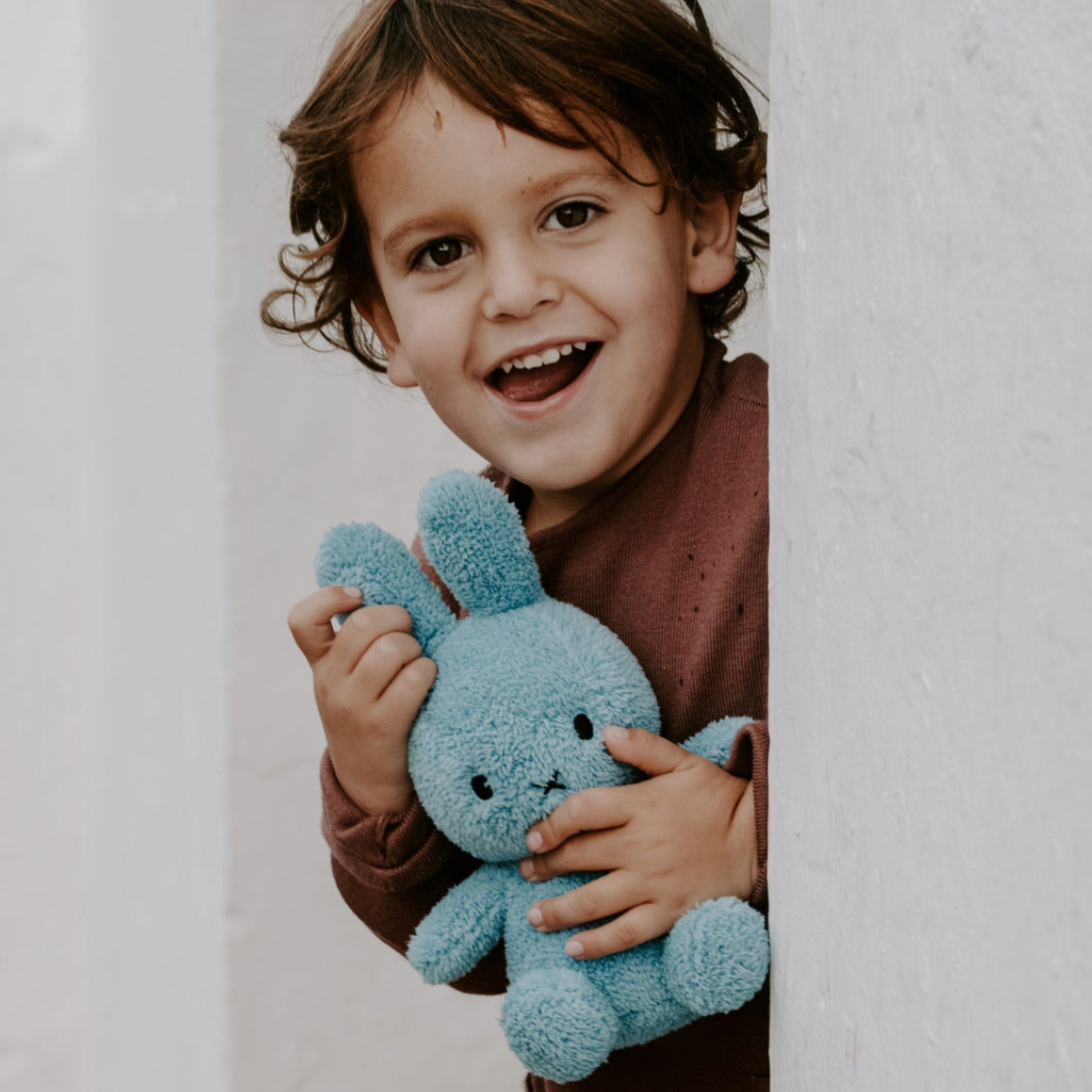 Child with light blue terry Sitting Miffy 23cm peering around coner with BonTon Toys Miffy in hand lifestyle shot