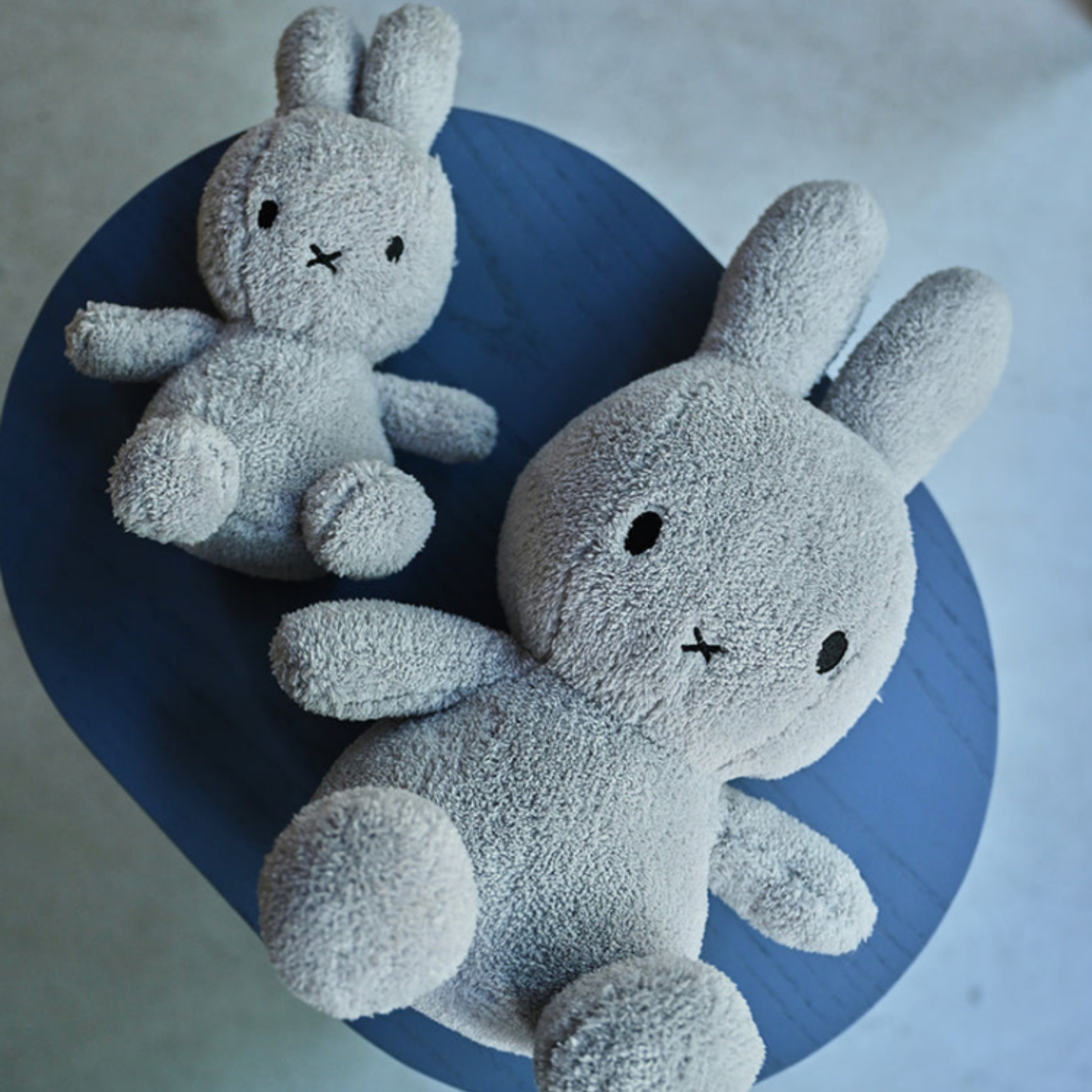 Blue table of two light grey Bon Ton Toys Miffys one large one small lying staggered lifestlye shot