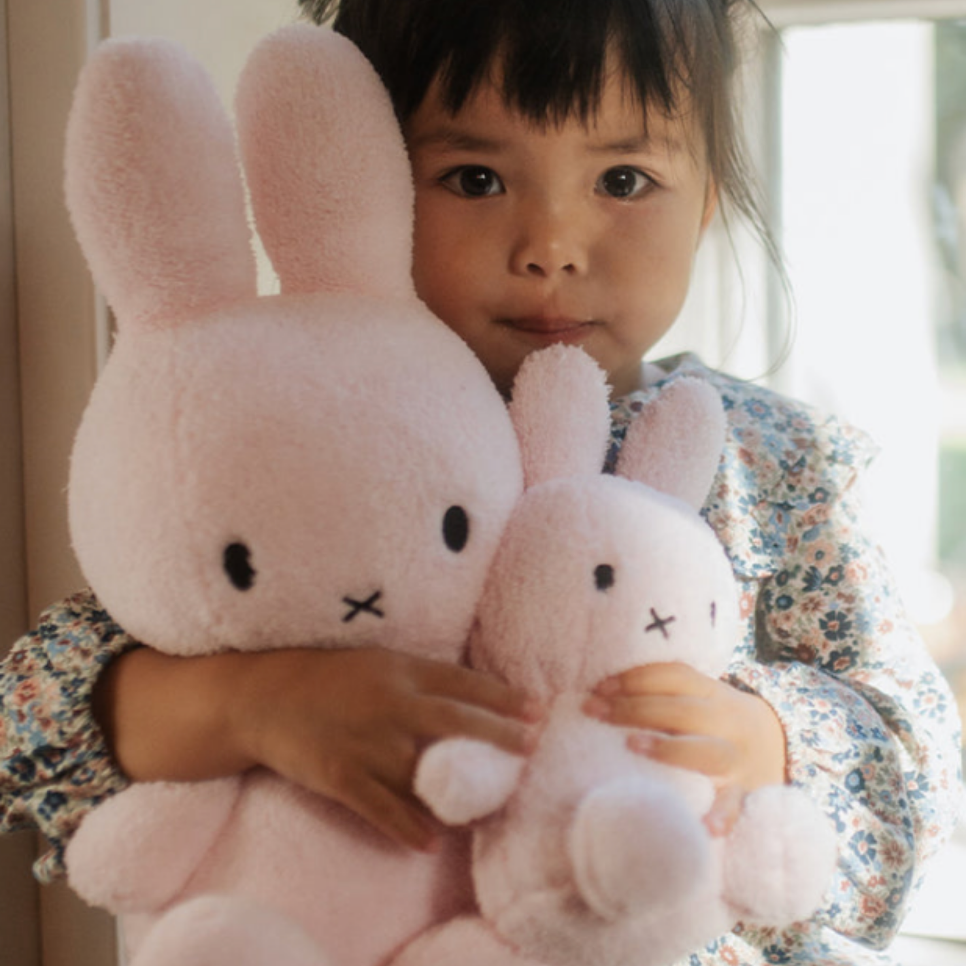 Close up of small girl holding light pink 23cm terry Bon Ton Toys Miffy and large terry Miffy in arms lifestyle shot