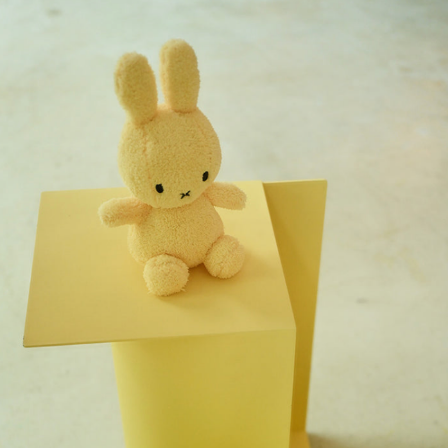 Light yellow terry Bon Ton Toys Sitting Miffy 23cm on yellow stand lifestyle shot