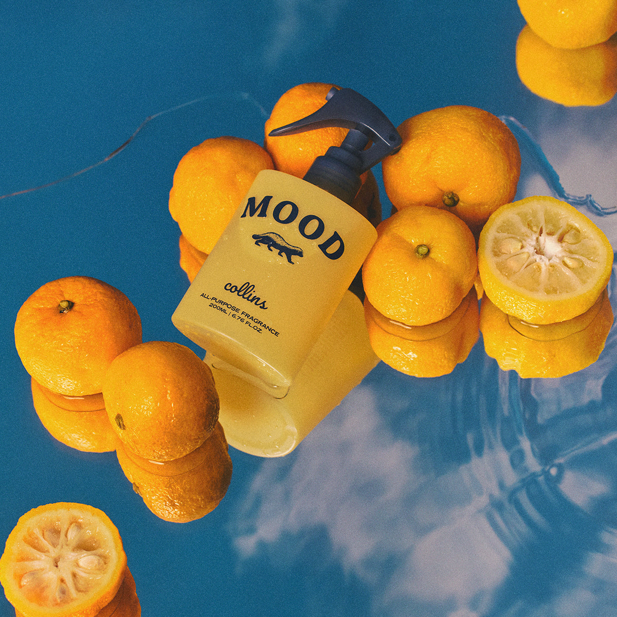 Collins Yuja 200ml water based Mood Water spray bottle laying on blue background with lemons