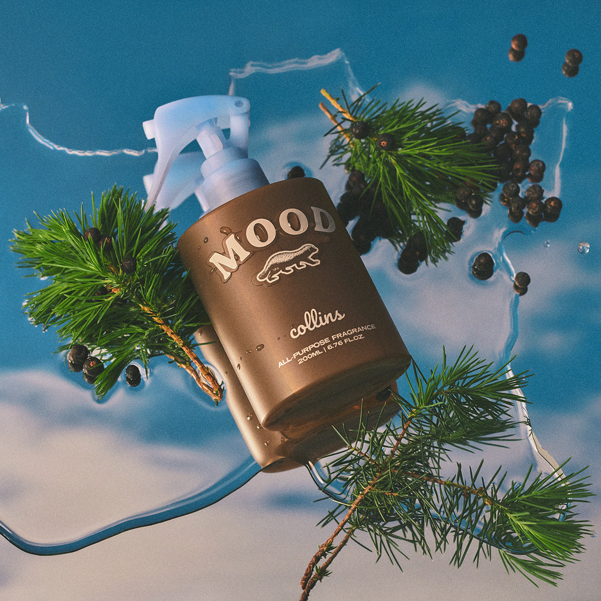 Collins Scottish Juniper 200ml water based Mood Water spray bottle laying on blue background with fir leaves and juniper berries