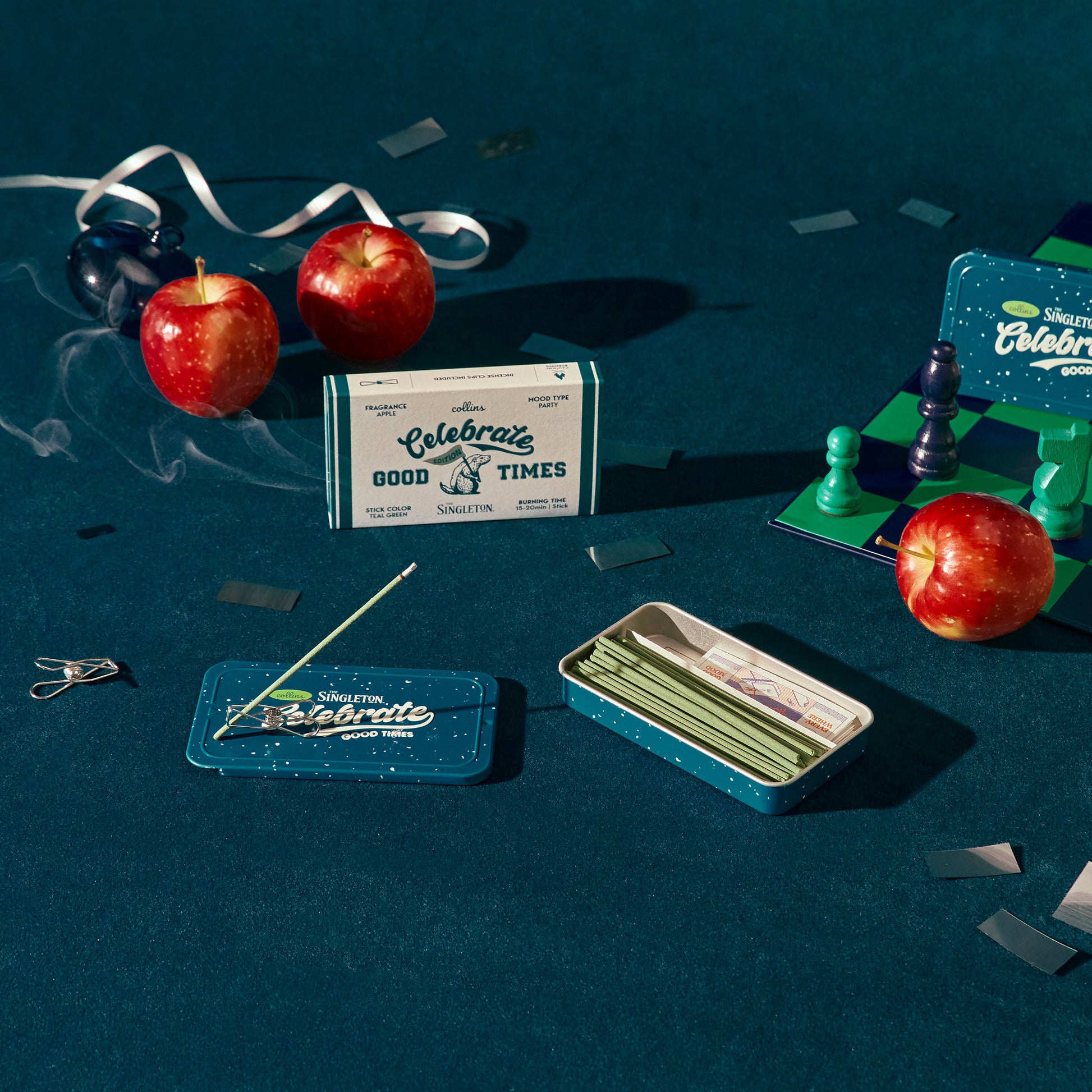 A tin of Collins natural incense sticks in good times scent, in a blue envirinmen with apples and a chess set.