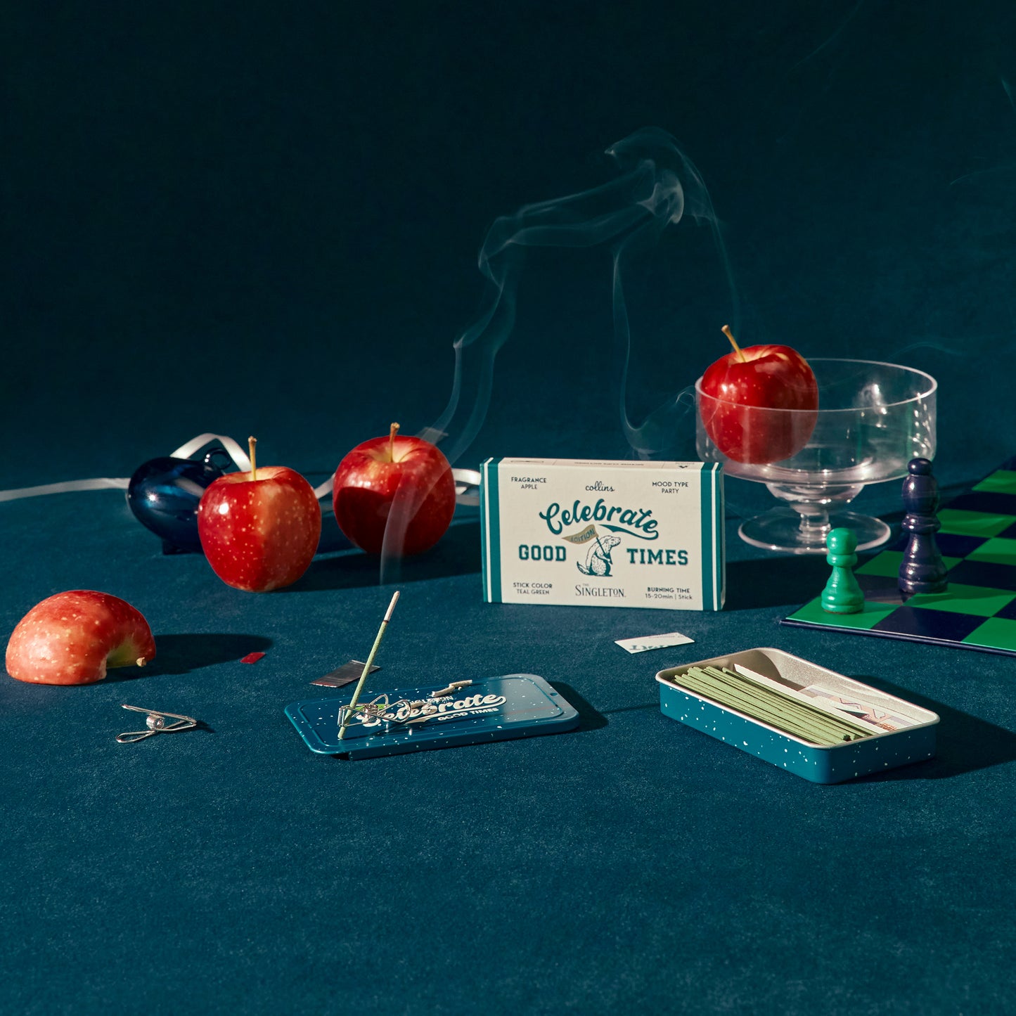 A tin of Collins natural incense sticks in good times scent in a blue envirinmen with apples and a chess set.