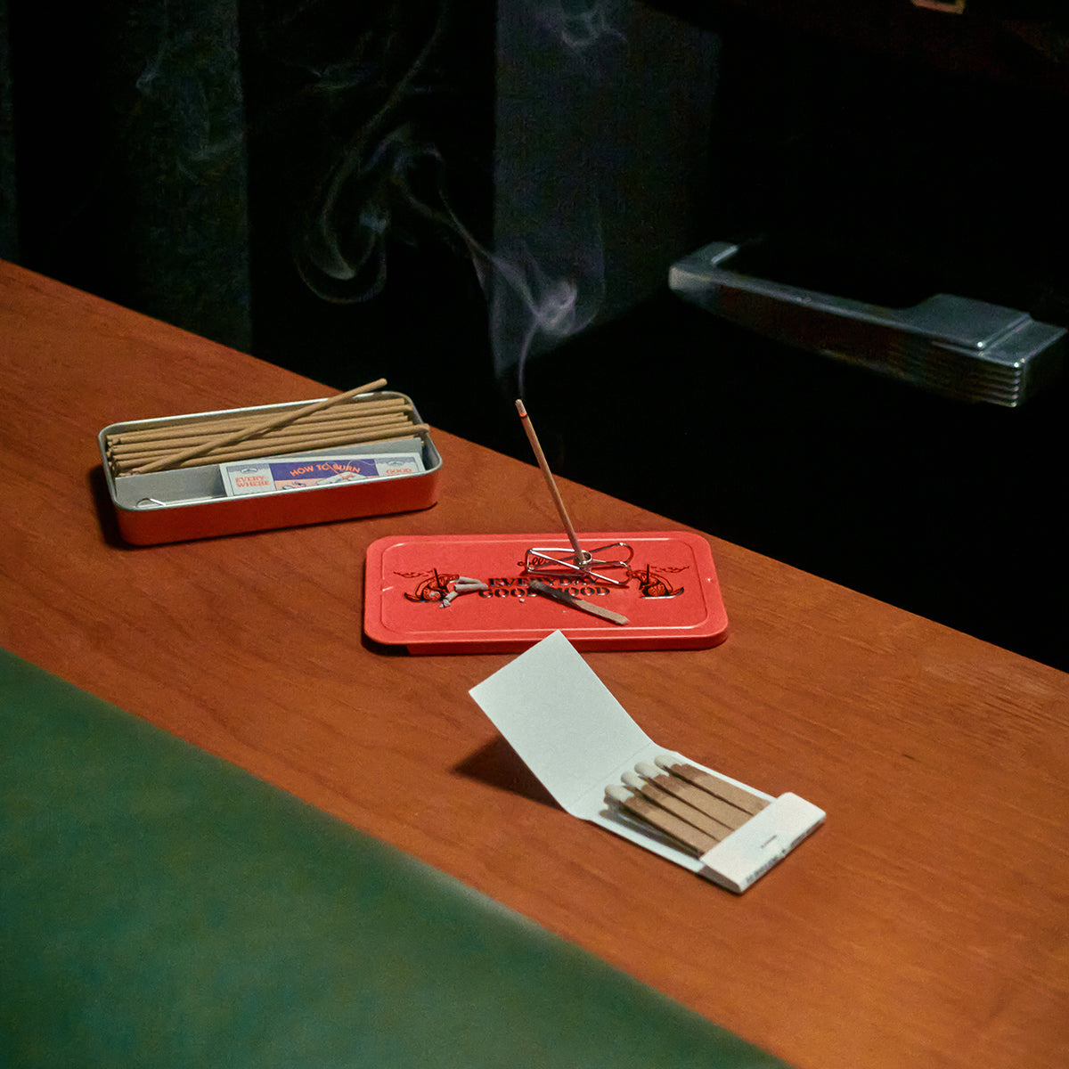Collins 'Welcome Drink' natural incense burning on the metal tin on a wooden table with matches