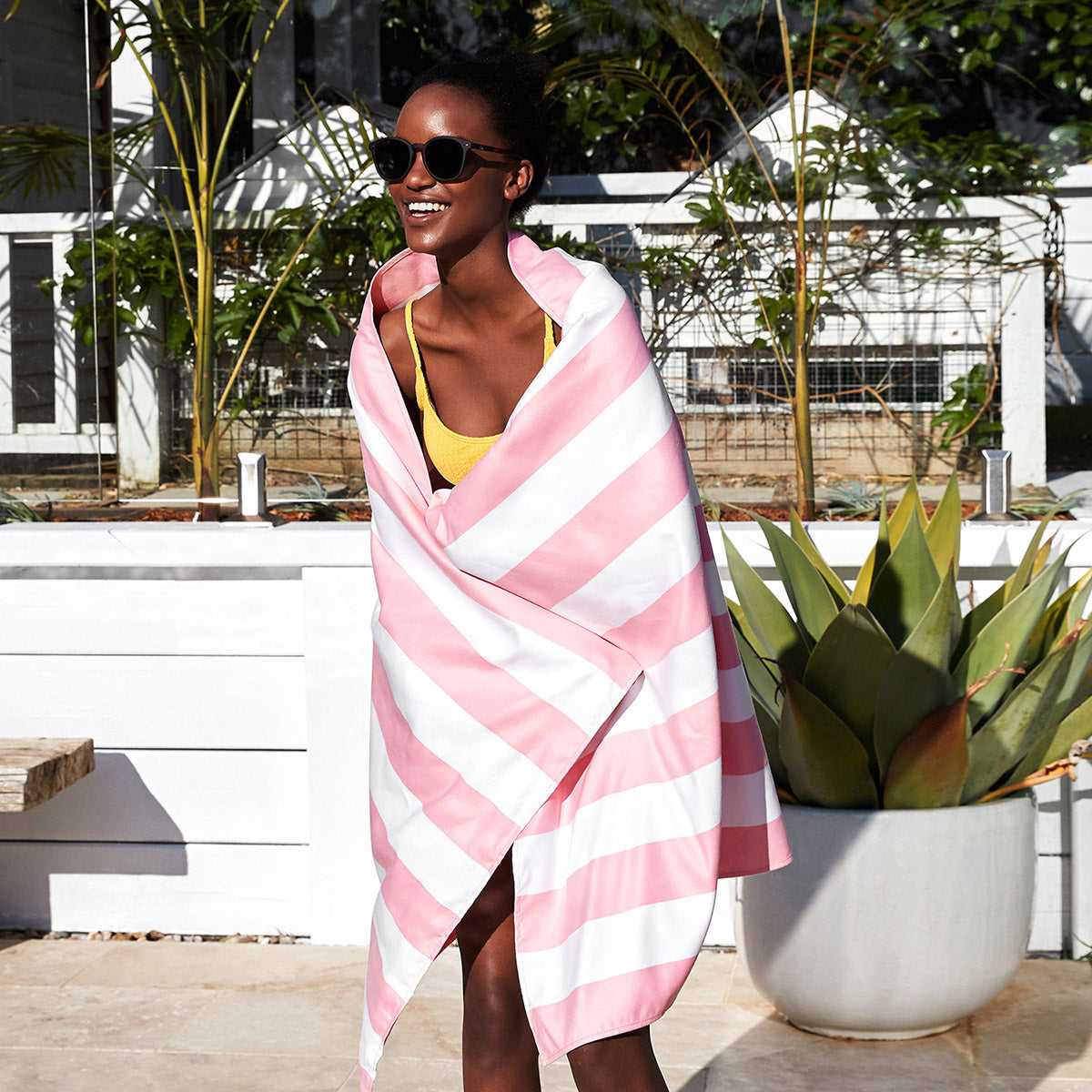 Dock and Bay malibu pink XL striped beach towel worn by woman wearing sunglasses in poolside scene 
