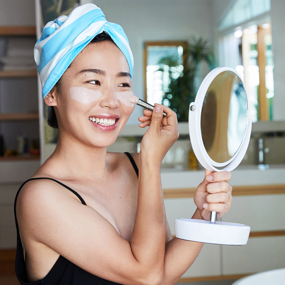 Woman wearing Dock and Bay Tulum Blue cabana stripe hair wrap and doing her makeup holding a white mirror