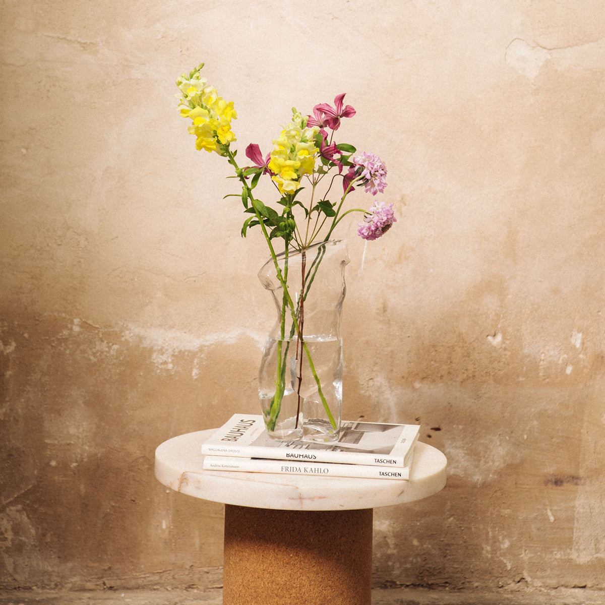 Doiy glass body vase on round marble table with yellow and pink flowers