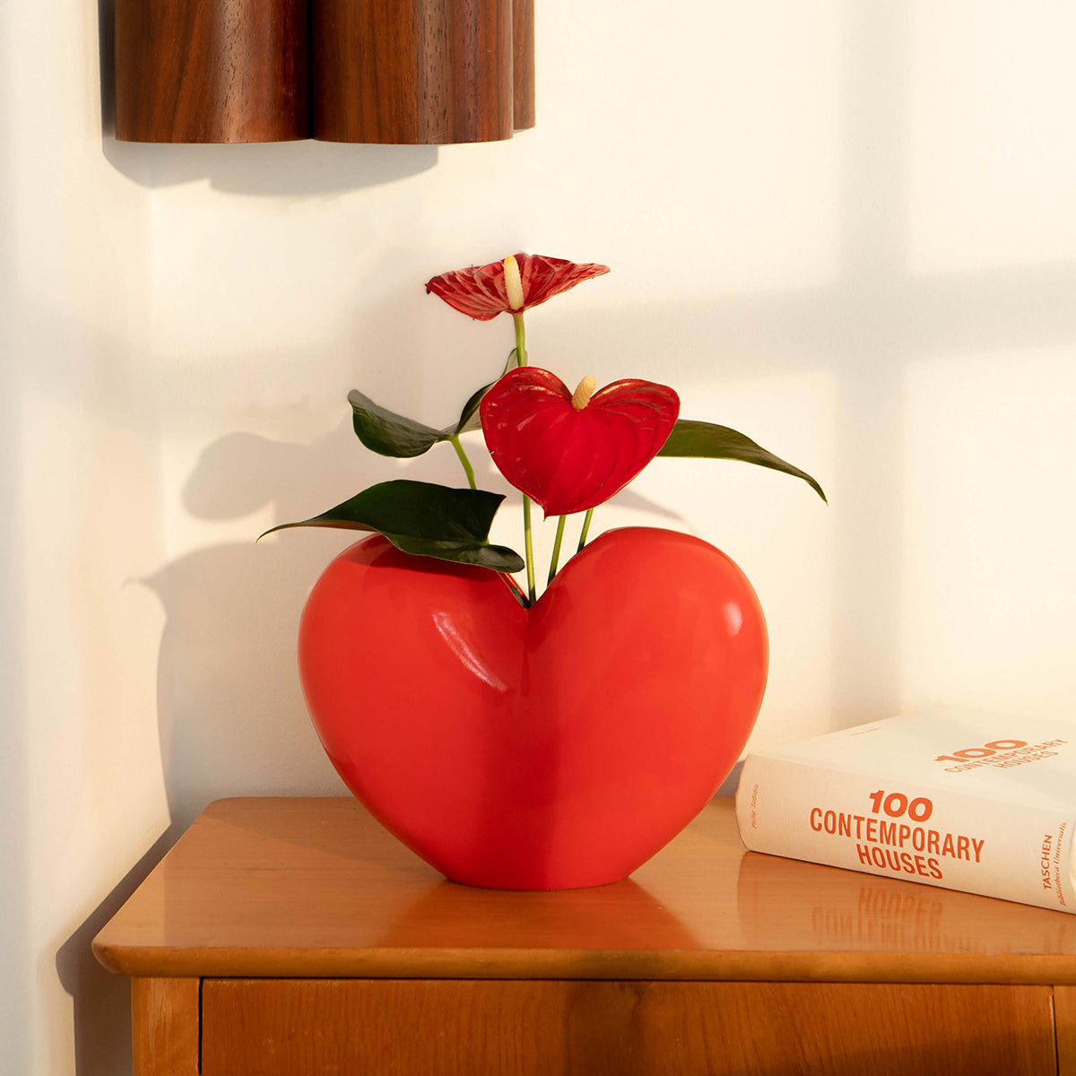 Red ceramic DOIY love vase filled with ginger lillies on wooden sideboard next to book on 100 contemporary houses