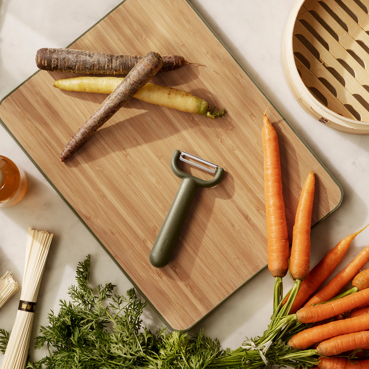 Eva Solo green tool Peeler resting on a chopping board with vegetables scattered around.