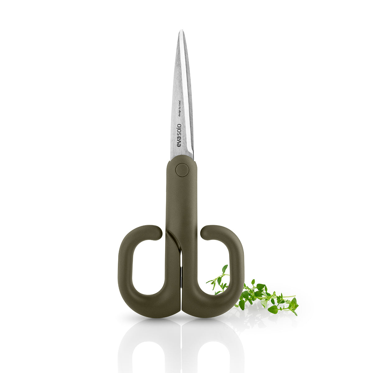 Green tool scissors by eva solo standing upright on its handle with oregano in background.