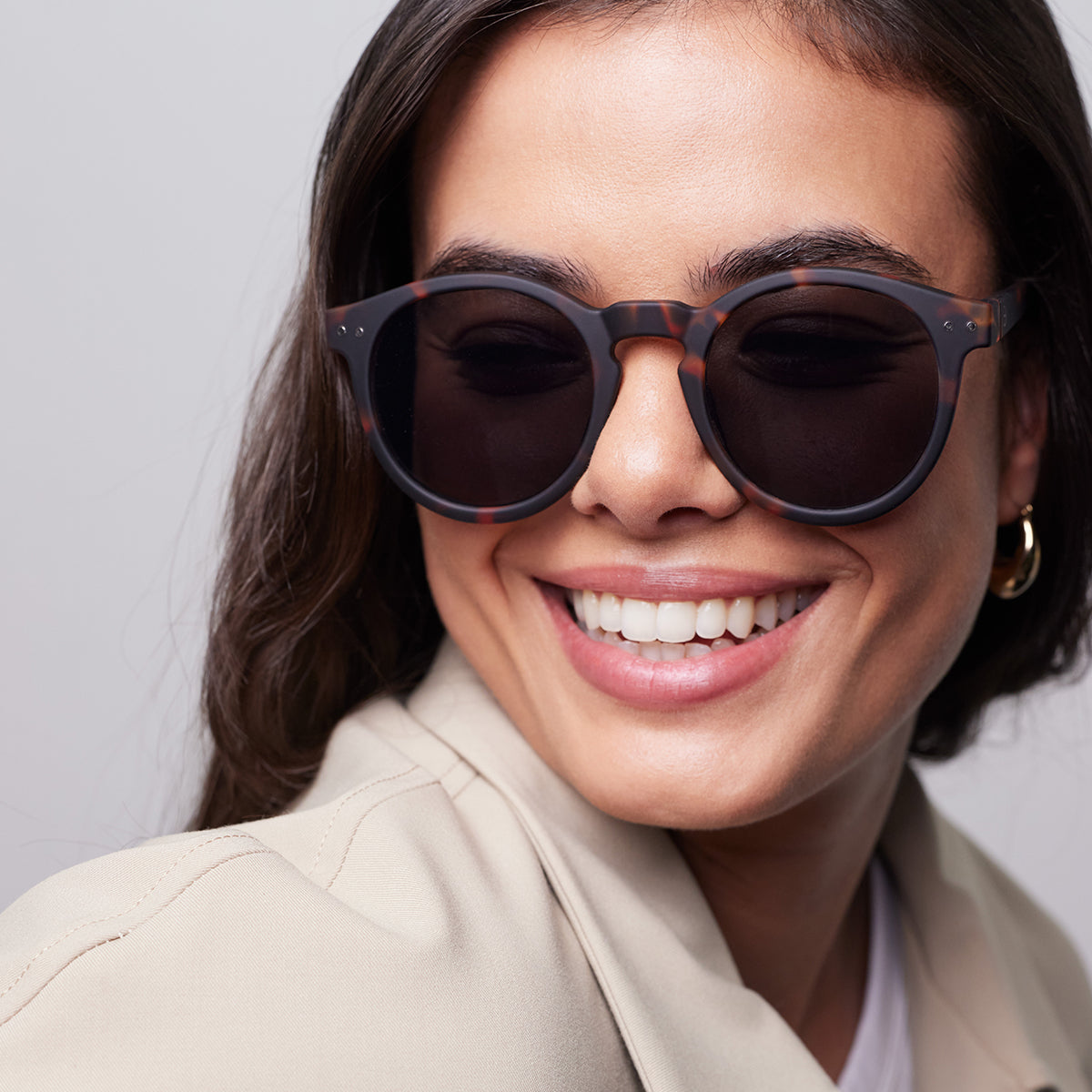 Close up of woman wearing Izipizi shape m tortoise sunglasses wearing a cream top looking over her shoulder 