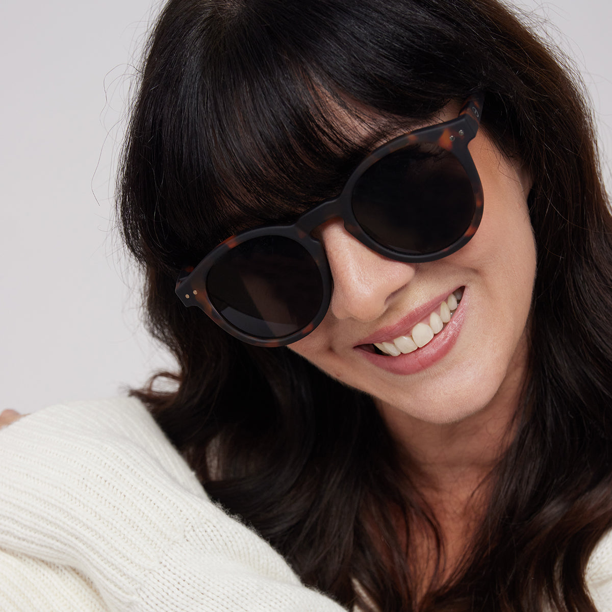 Close up of woman wearing Izipizi shape n tortoise sunglasses wearing a cream top with head tilted down