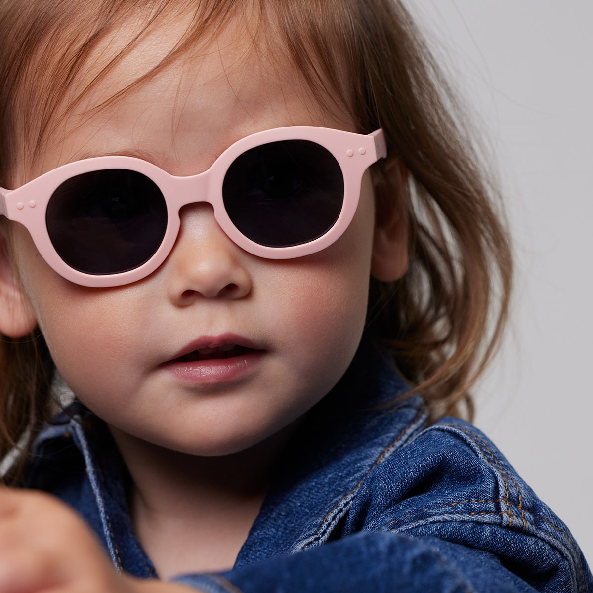 Little girl in denim jacket wearing Izipizi kids sunglasses shape c pastel pink