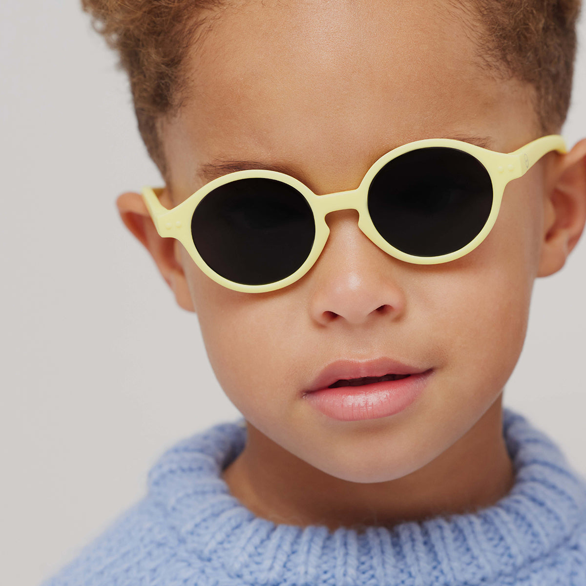 Little boy in blue knitted jumper wearing Izipizi kids sunglasses shape d lemondade
