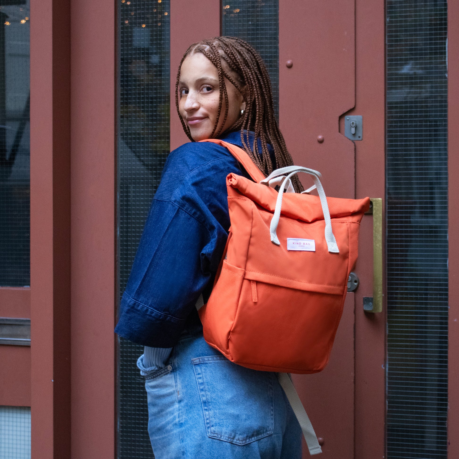 Kind Bag's Backpack Medium in colour burnt orange shown slung over a woman's shoulder.