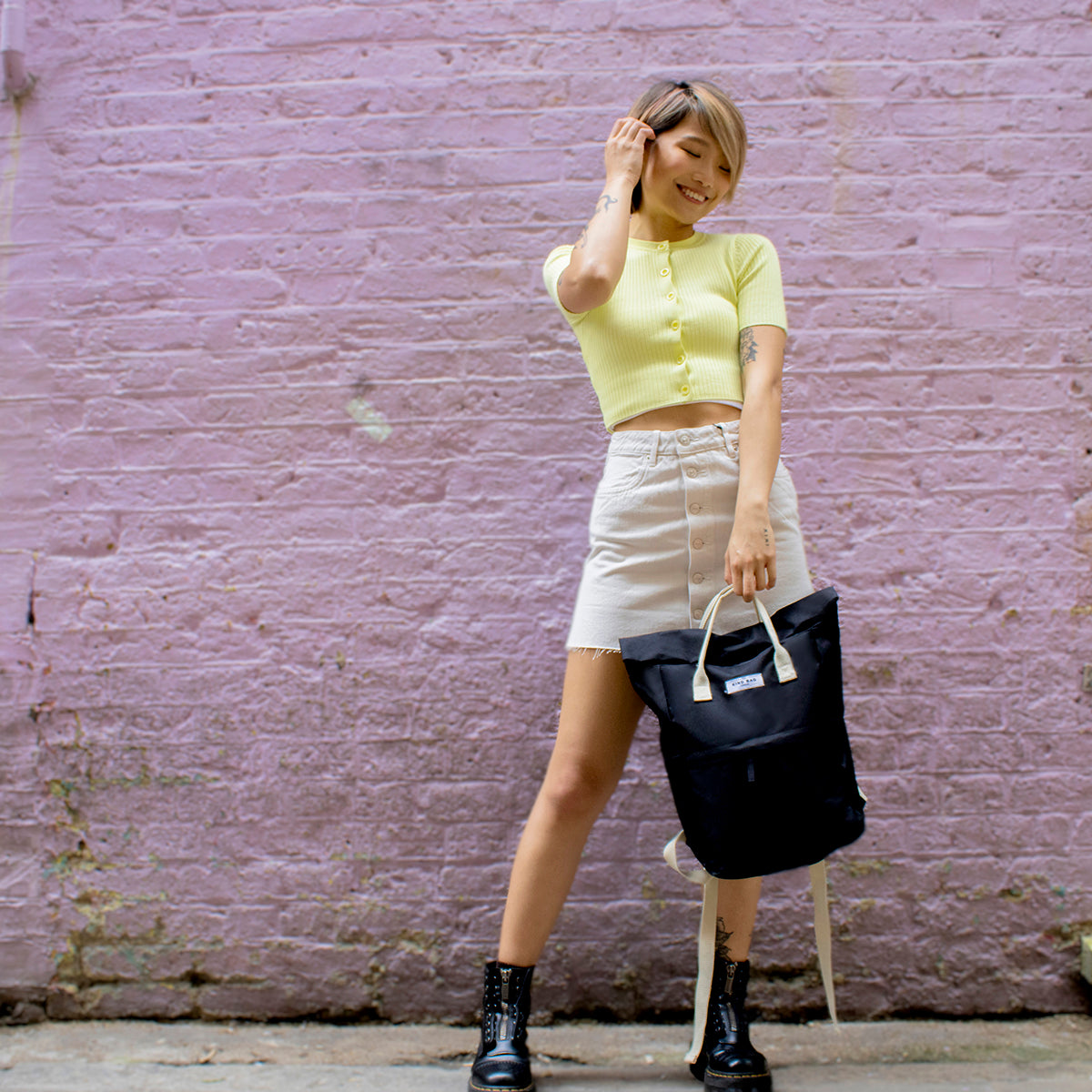 Kind Bag's Backpack Medium in colour black shown being held by its top handle by a woman.