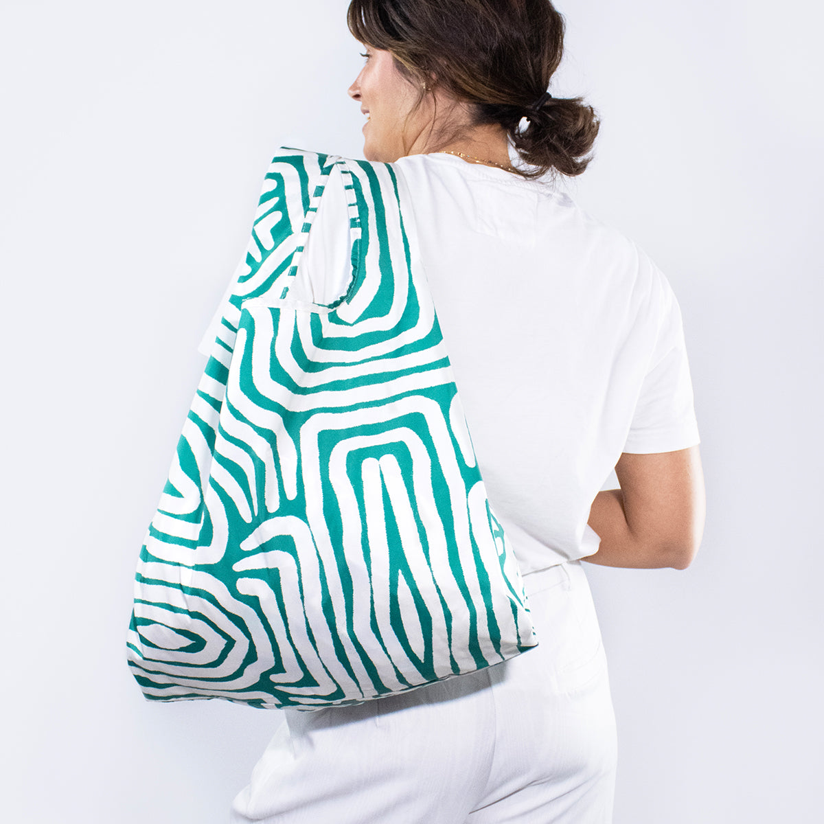 Image showing Regusable bag by Kind bag in green and white abstracted lines print, shown slung over a woman's shoulder.