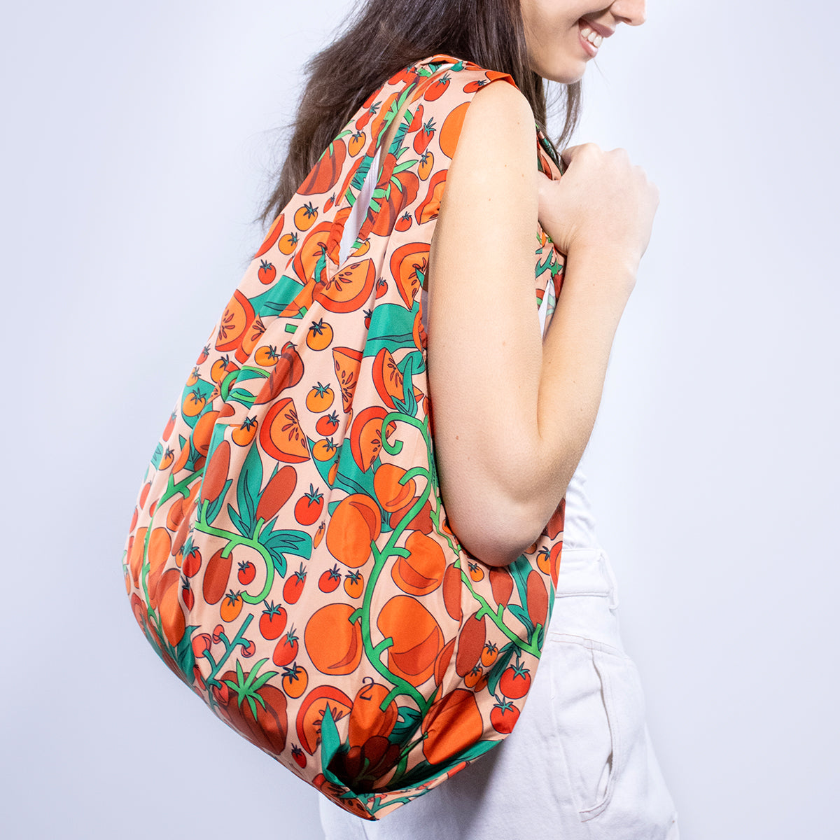 Image showing Regusable bag by Kind bag in vibrant tomato print, shown slung over a woman's shoulder.