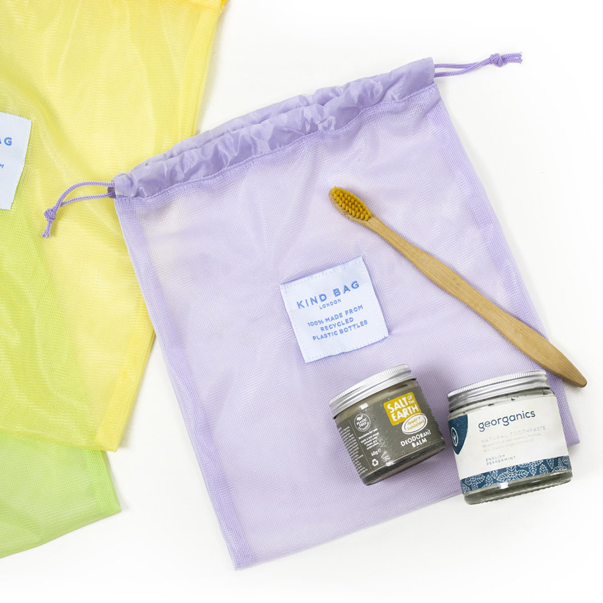 Image showing purple bag from set of 3 Regusable Mesh bags by Kind bag in flat lay format with toiletries.