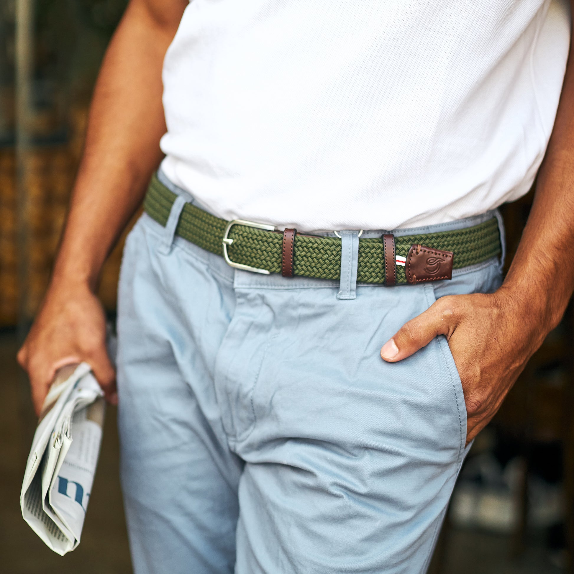 Man wearing La Boucle mono edinburgh woven belt around pale blue pants and white t-shirt holding a newspaper