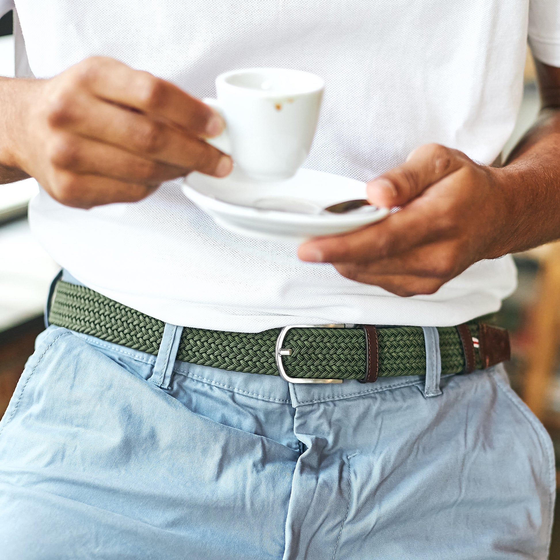 Man wearing La Boucle mono edinburgh woven belt around pale blue pants and beige white tshirt drinking espresso coffee