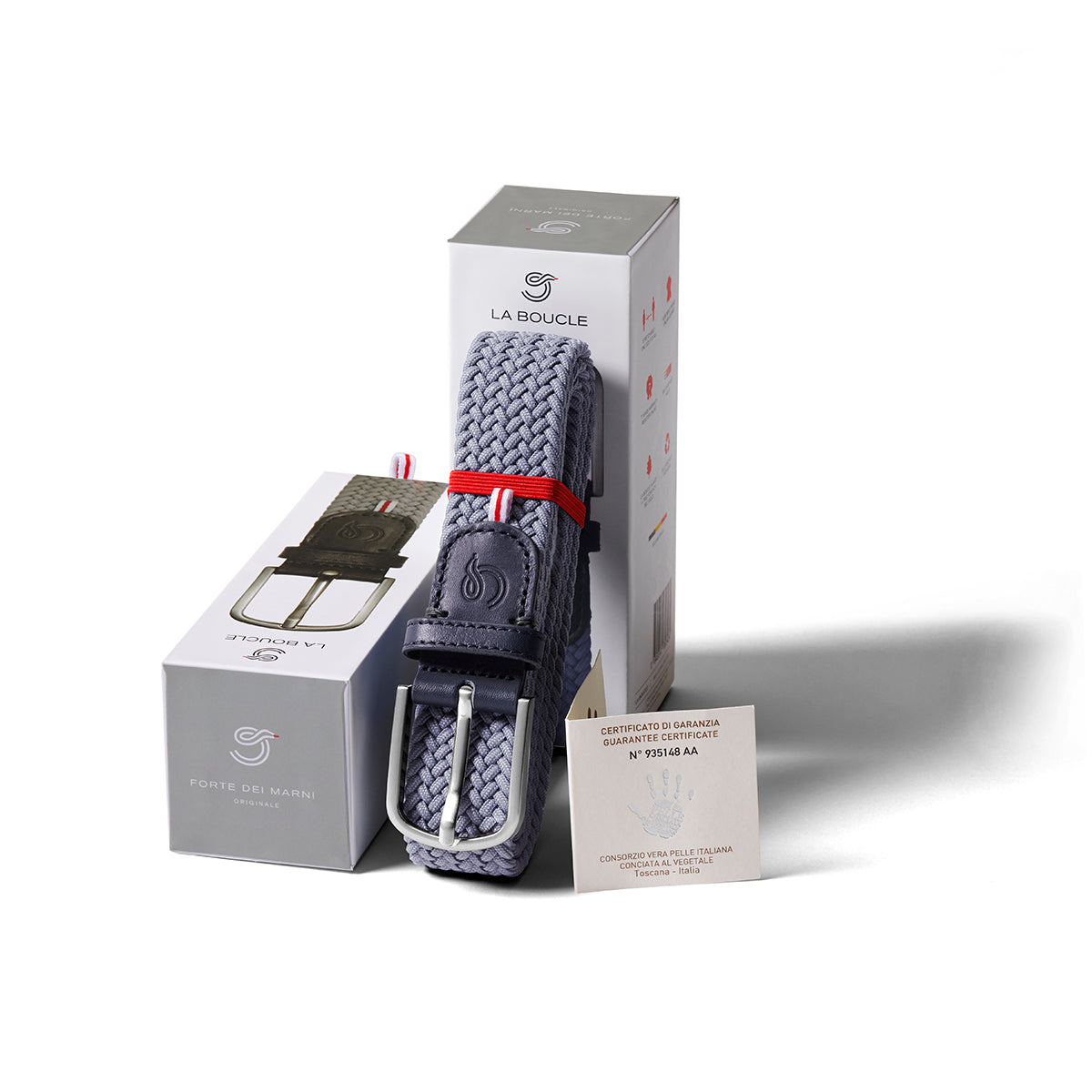 La Boucle mono forte dei marmi woven belt folded and leaning on a box next to a box on white background