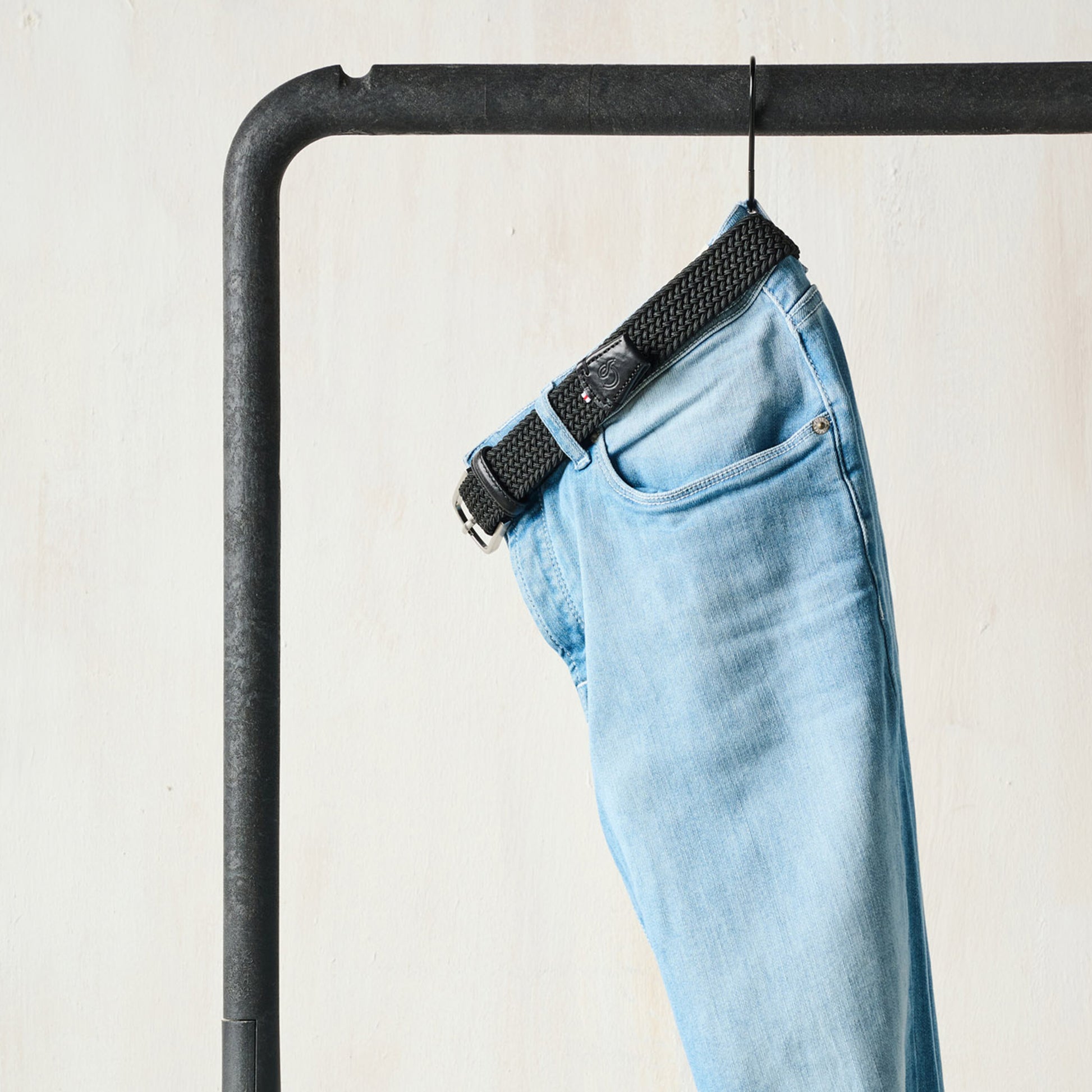 La Boucle mono London woven belt threaded through pale denim jeans hanging on rack
