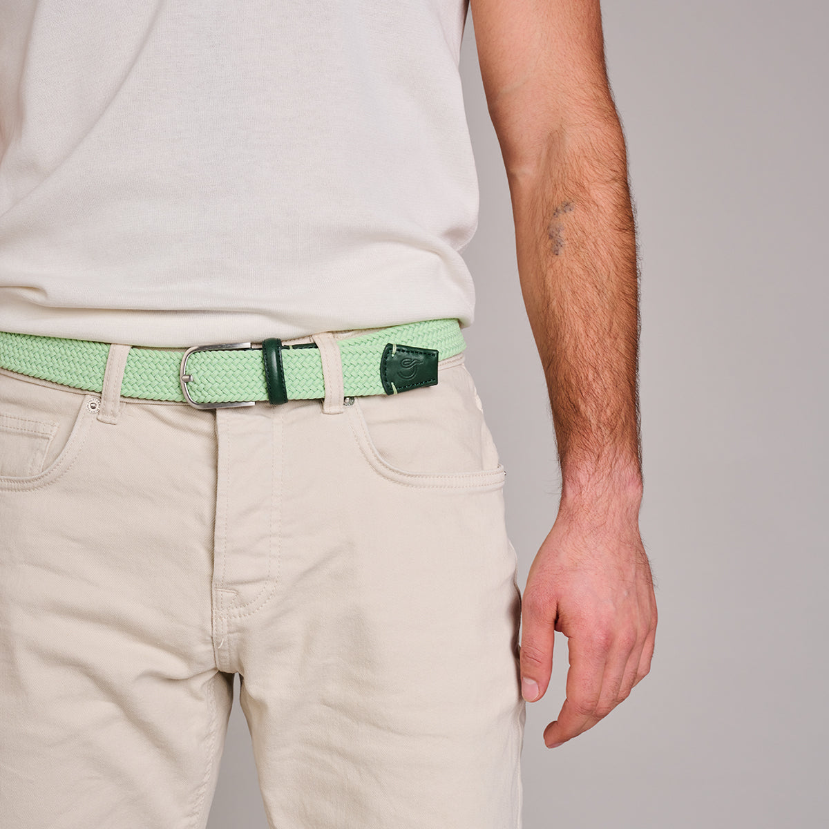 Man wearing La Boucle Mykonos woven belt around beige pants and white tshirt on grey background