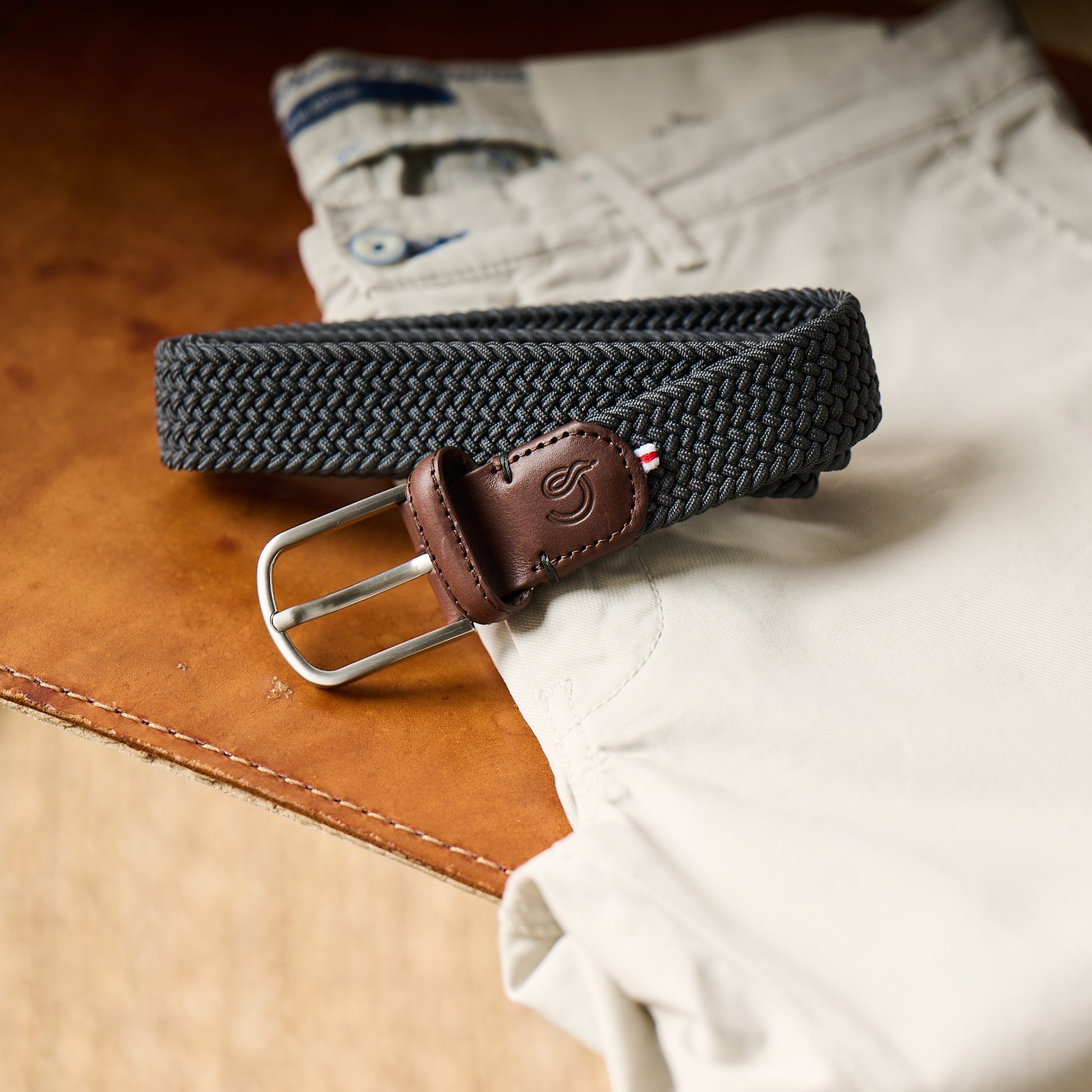 La Boucle mono New York woven belt folded on beige pants on table
