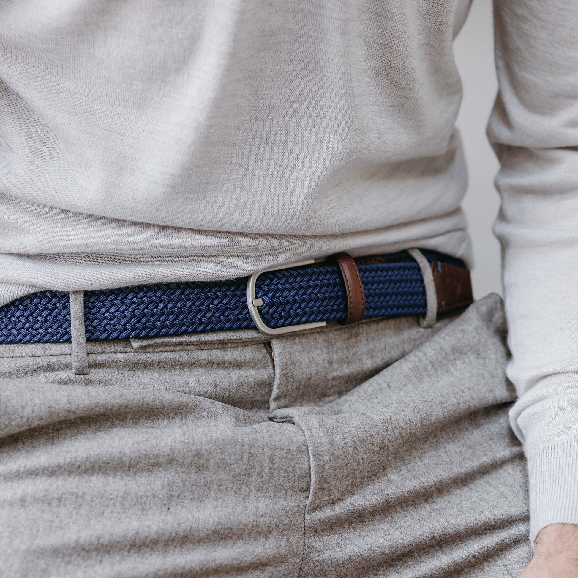 Close up of man wearing La Boucle mono Paris woven belt around pale grey pants, cream long sleeve top