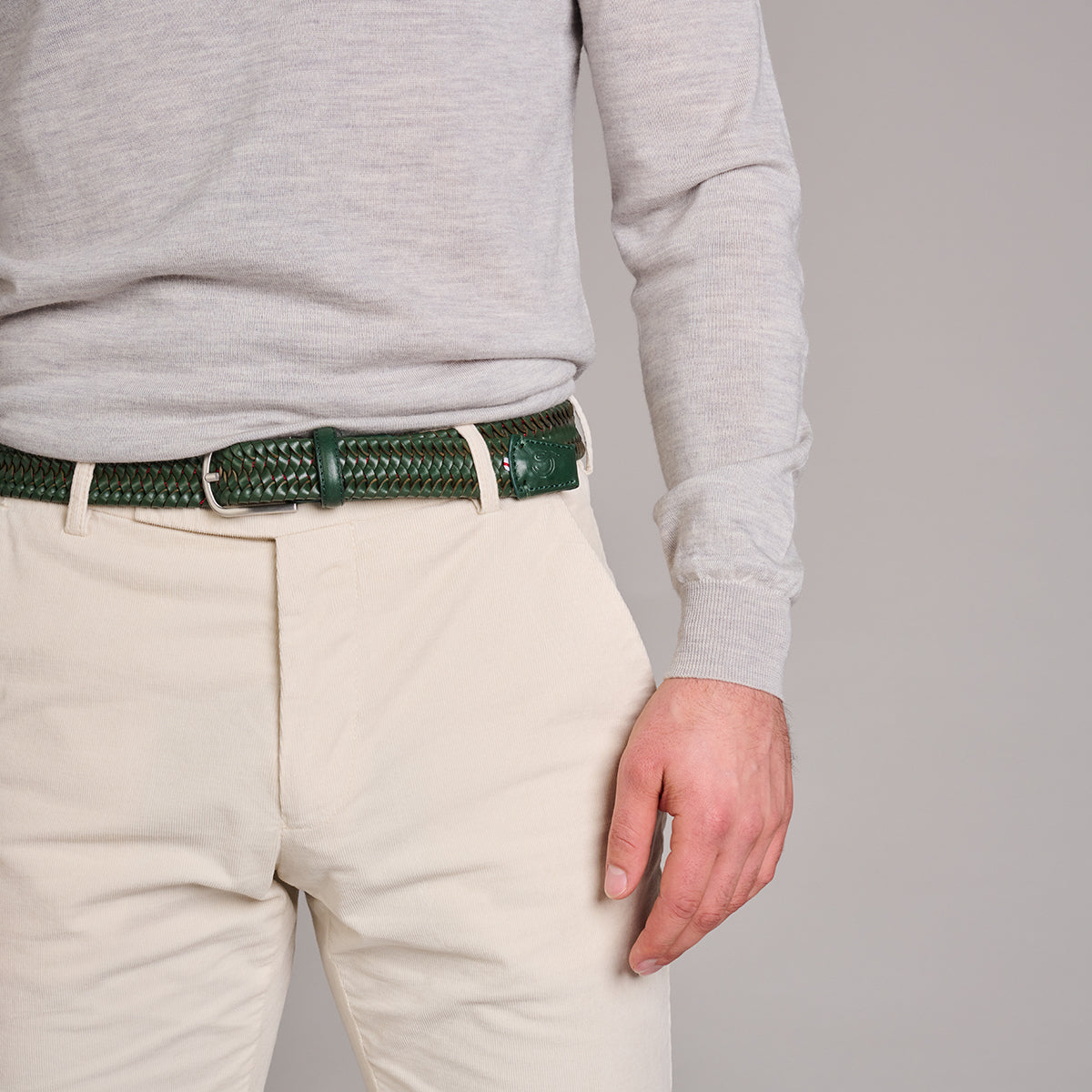 Close up of man wearing La Boucle stretch leather mono Genoa woven belt around cream pants and grey top on grey background