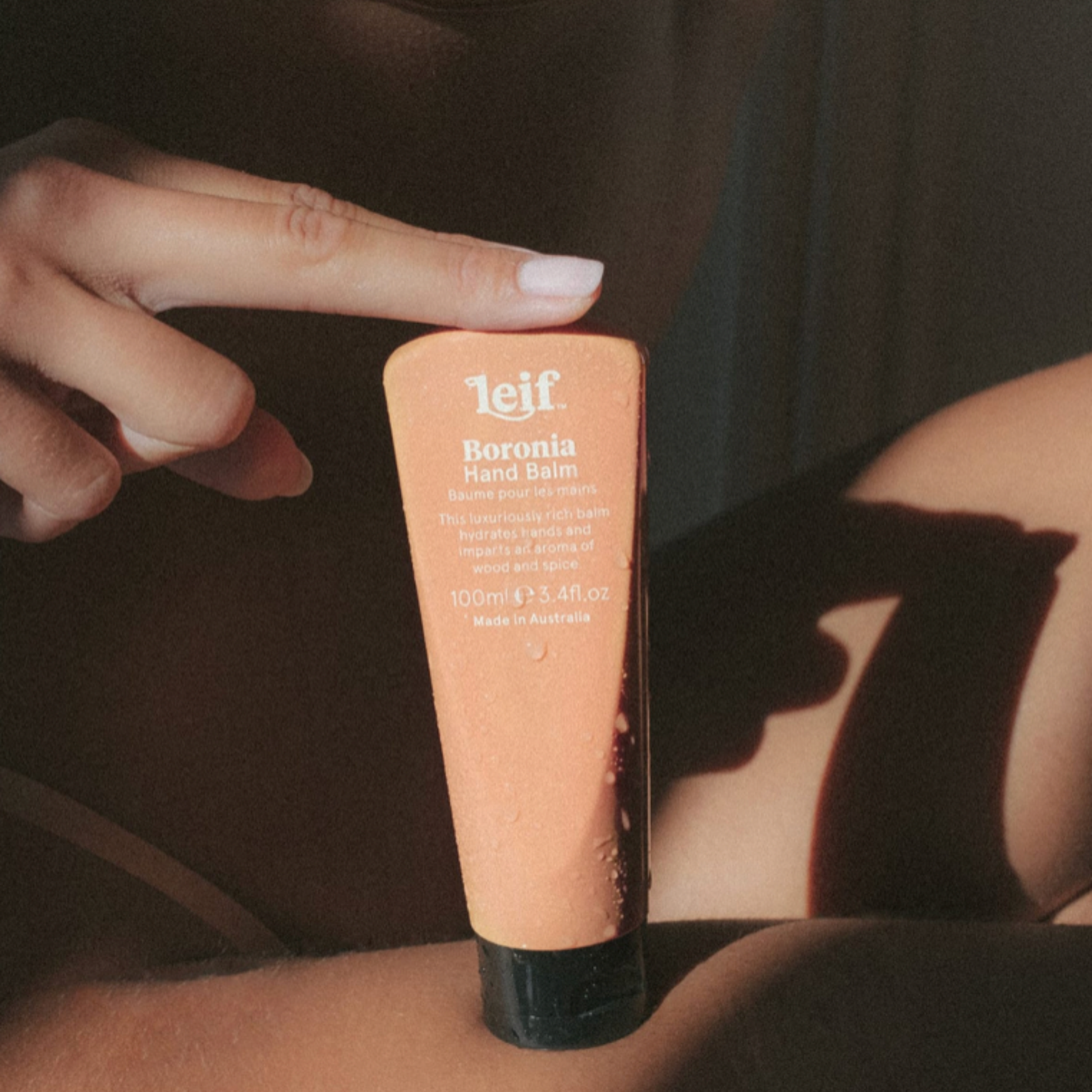 Woman holding Leif hand balm 100ml Boronia between her fingers and legs 