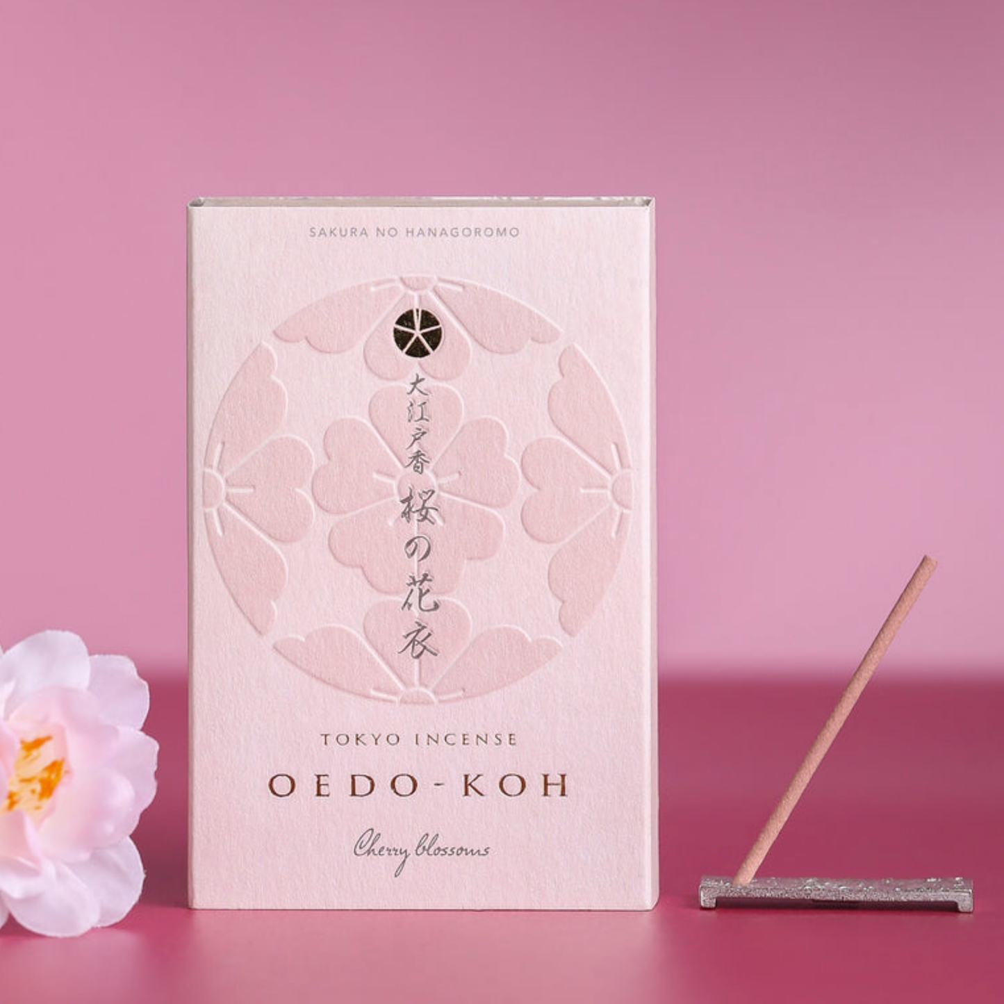 Oedo-Koh Incense Cherry Blossoms on display with incence out of packaging stood in included incense stand next to box with pink background and a cherry blossom beside