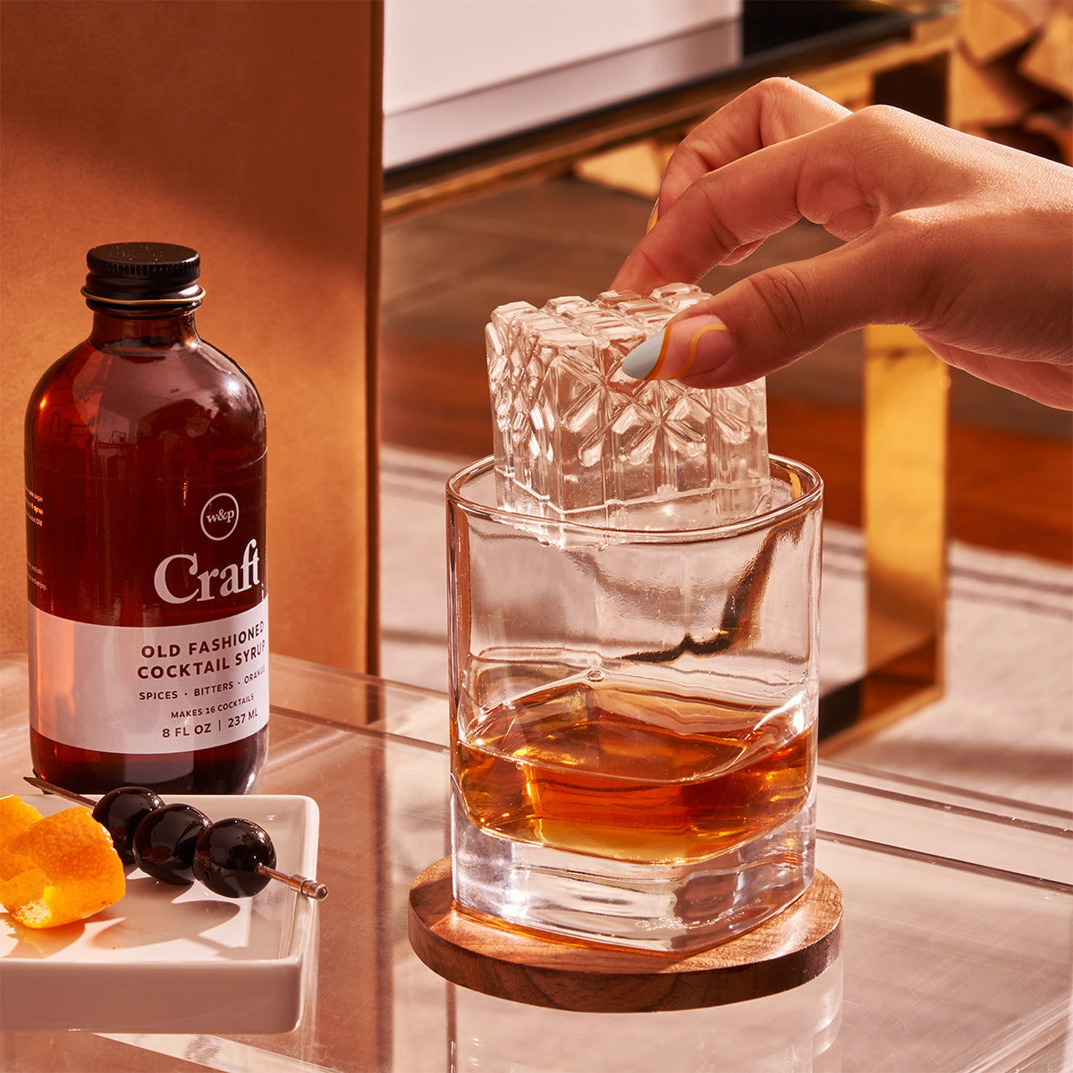 WP charcoal crystal cocktail ice cube in whiskey glass sitting next to craft cocktail mix 