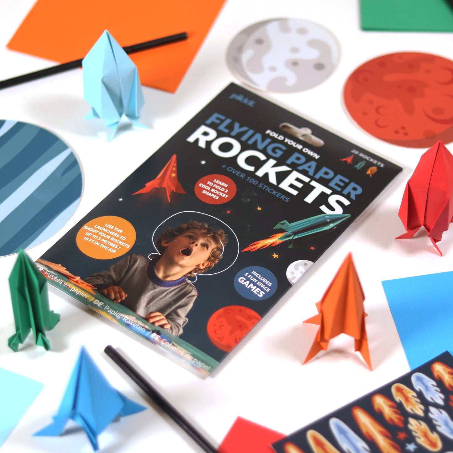 Colored paper rockets from Pikkii Flying Paper Rockets kit - DIY paper rocket craft set in multi-color FSC-style printed sheets, includes materials for 20 foldable rockets in 3 shapes, blow launchers, 100+ stickers, and step-by-step instructions; lightweight fun craft kit for kids ages 6+.